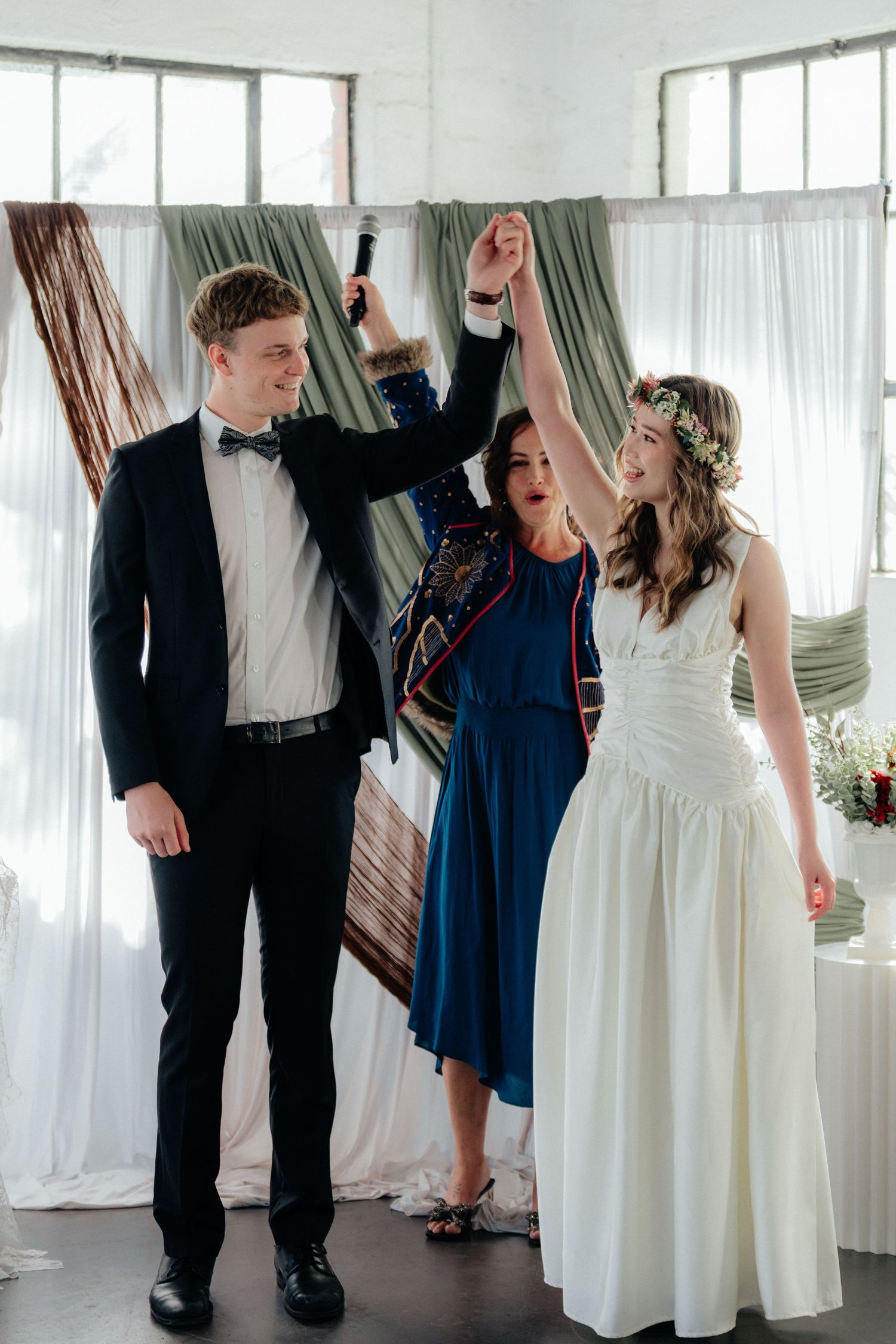 Joyful wedding officiant raises hands of smiling bride and groom after ceremony pronouncement.