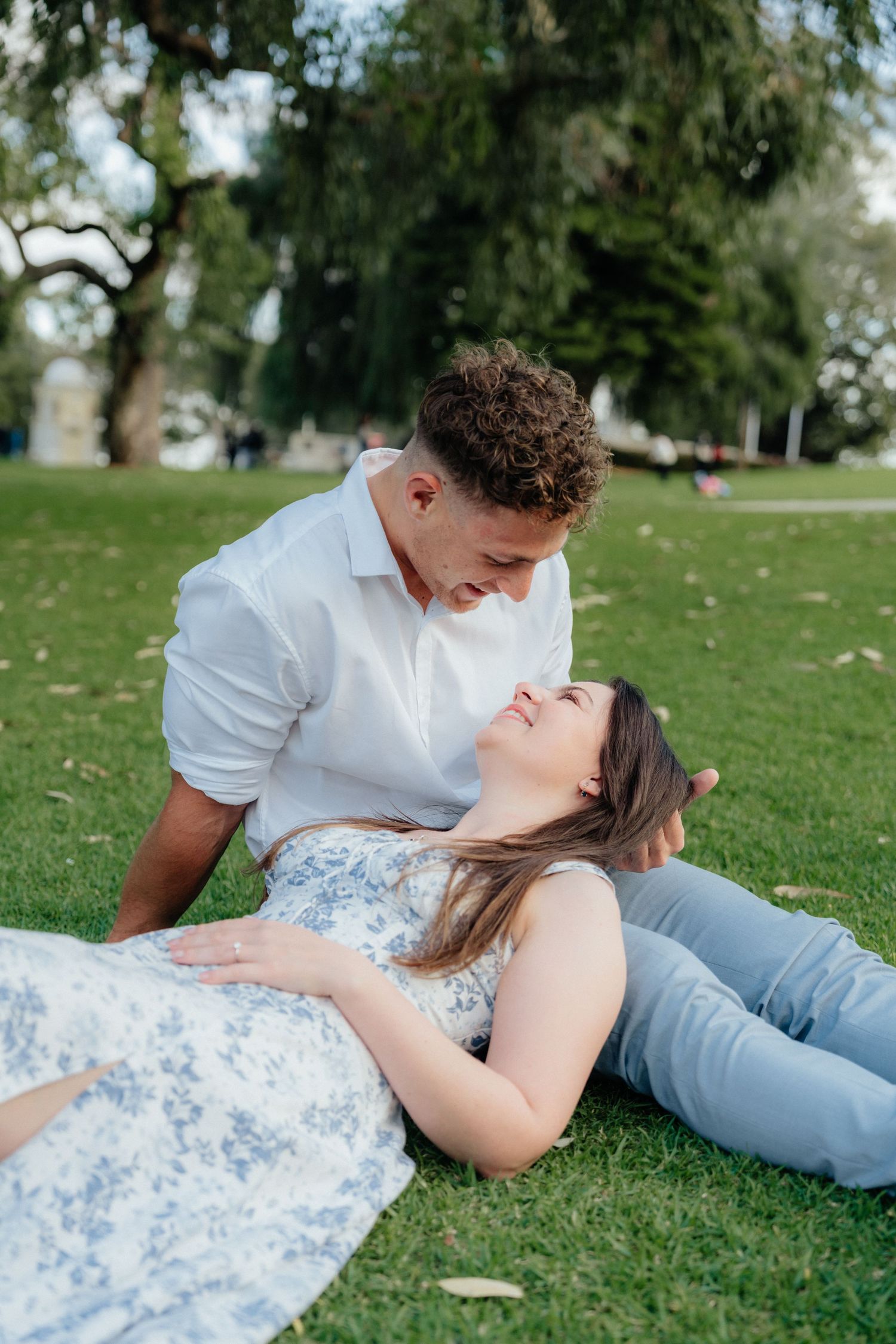 Romantic couple sharing a tender moment on grass in a park, woman lying in mans lap.