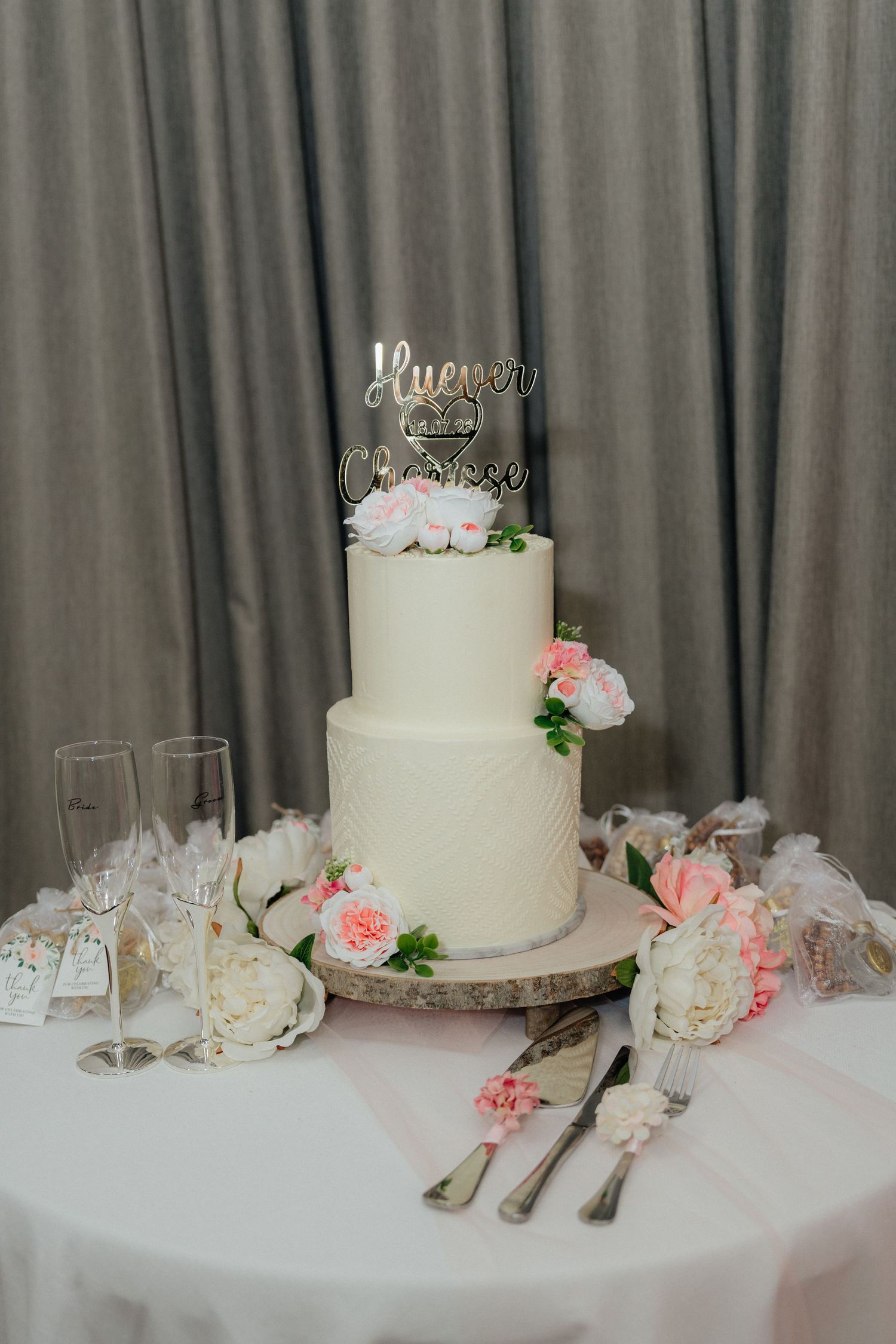 A two-tier white wedding cake with pink floral decorations and a personalized cake topper.