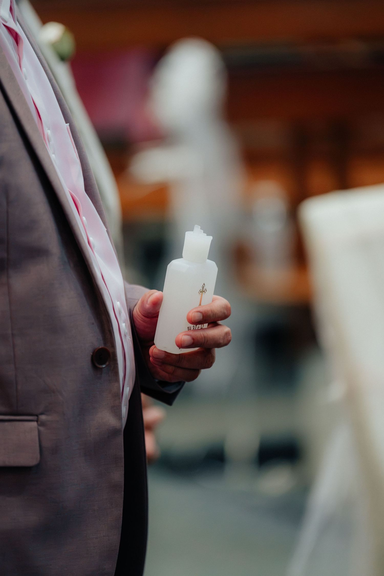 A man in a gray suit holds a white unity candle during a wedding ceremony.