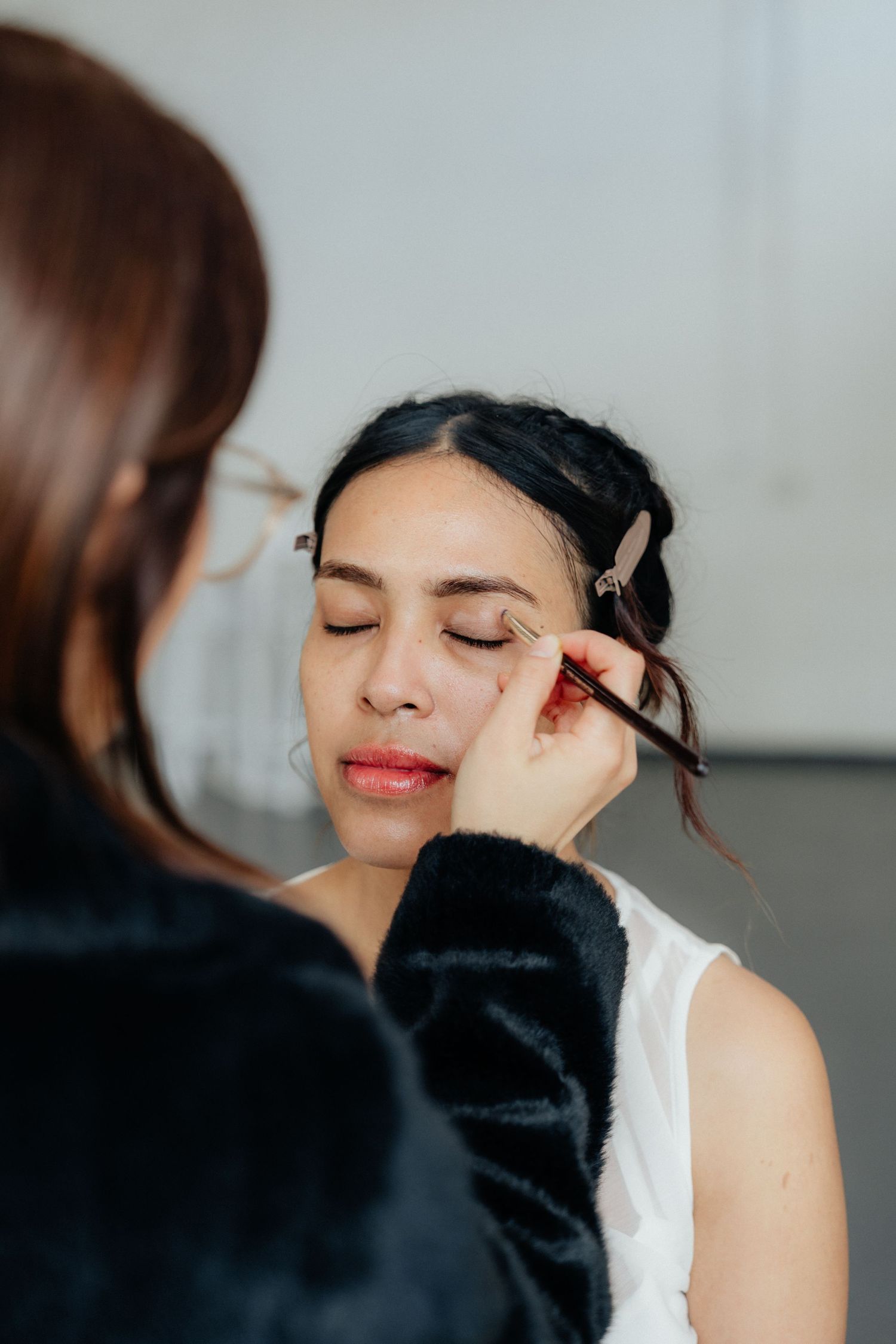 Makeup artist applying eyeshadow to a bride with dark hair in a white dress.