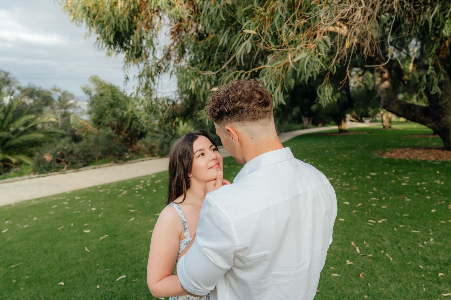 Romantic couple sharing tender moment together in lush green park with trees in background.