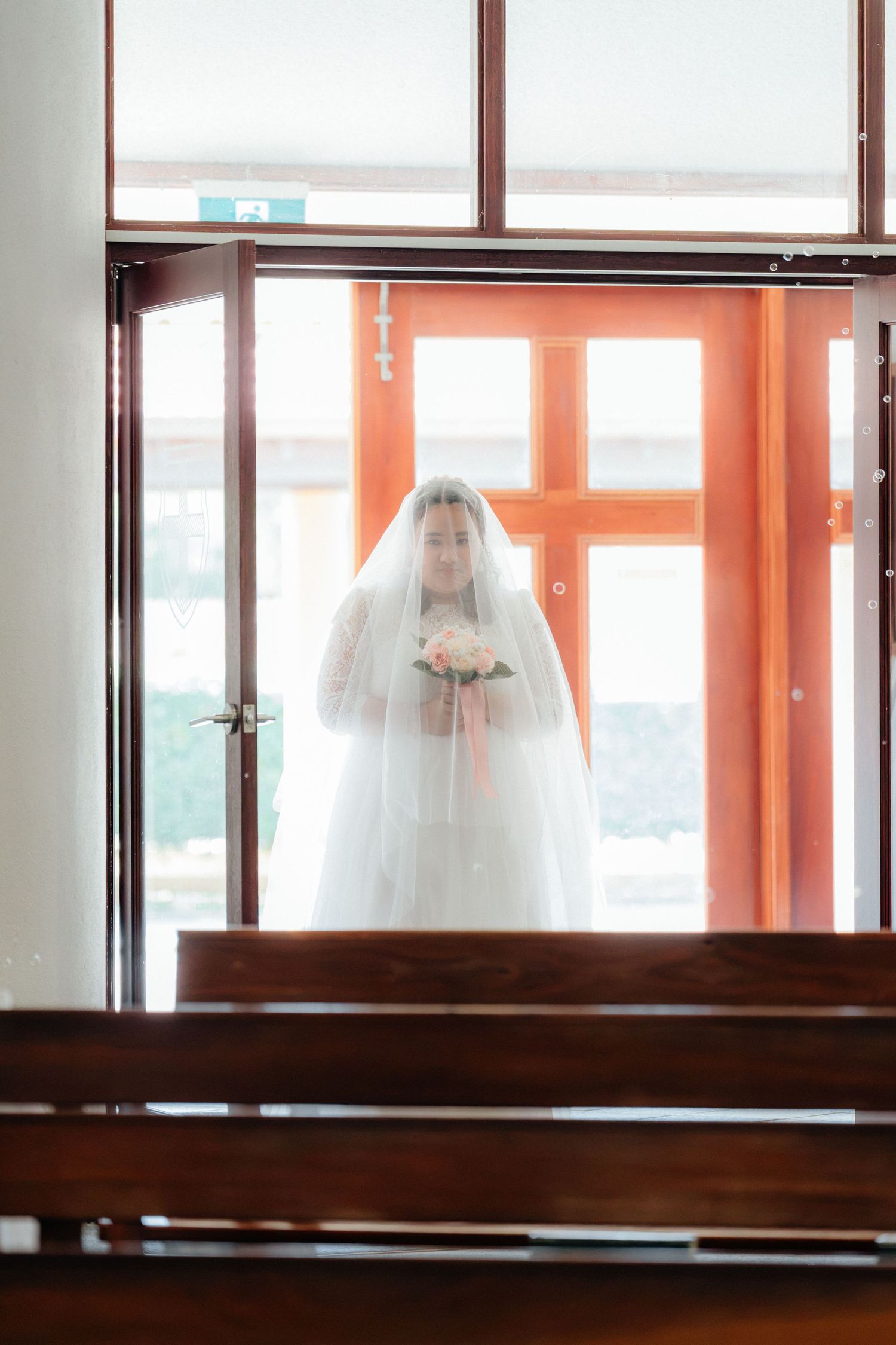 Bride in white gown and veil holding bouquet standing at church entrance before walking down the aisle.