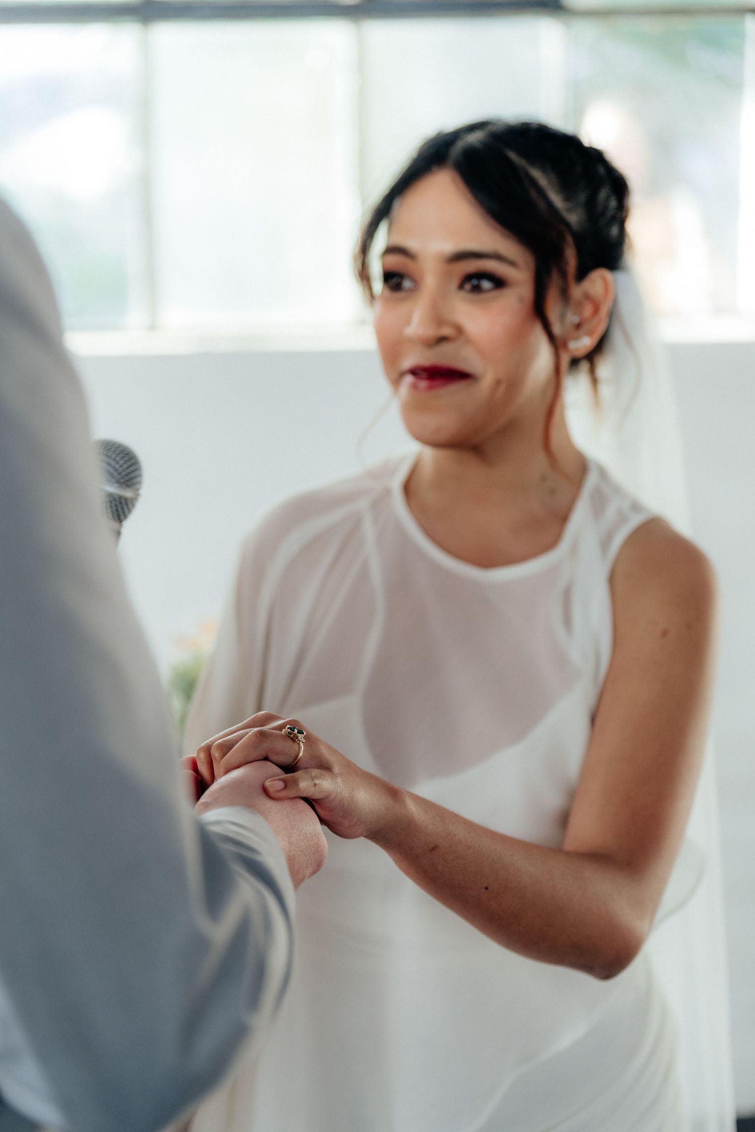 Bride in white dress placing a gold wedding ring on grooms finger during ceremony.