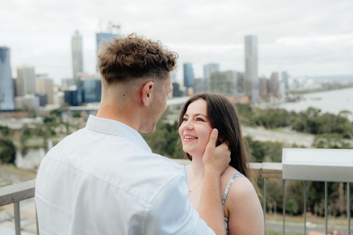 Couple sharing a romantic moment on a balcony overlooking a stunning city skyline.
