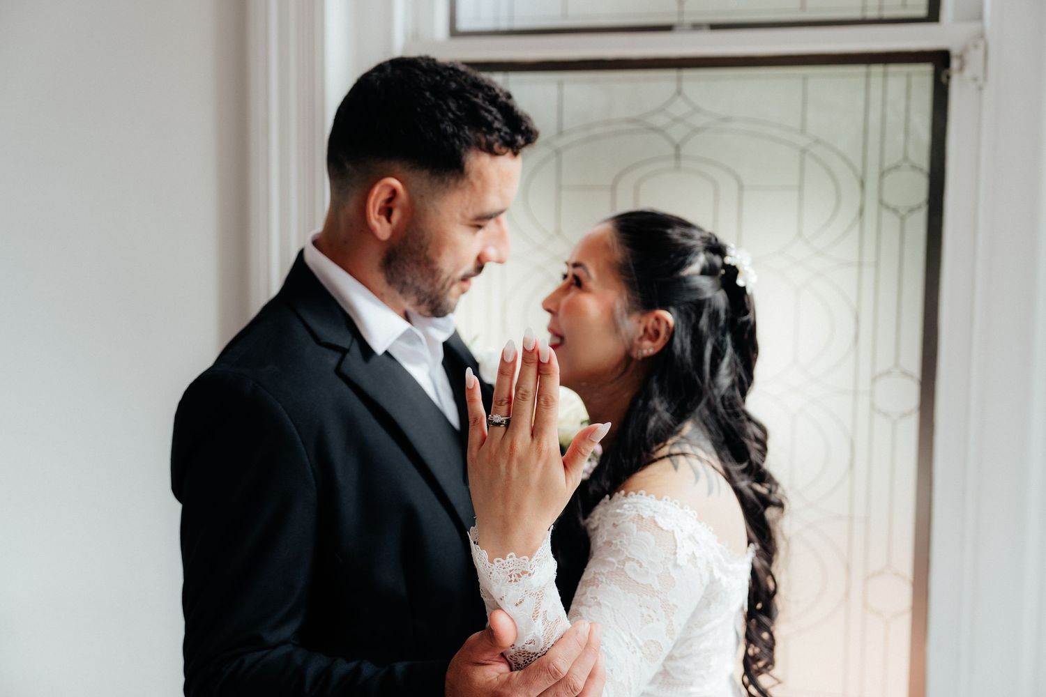 A bride and groom share an intimate moment near a stained glass window on their wedding day.