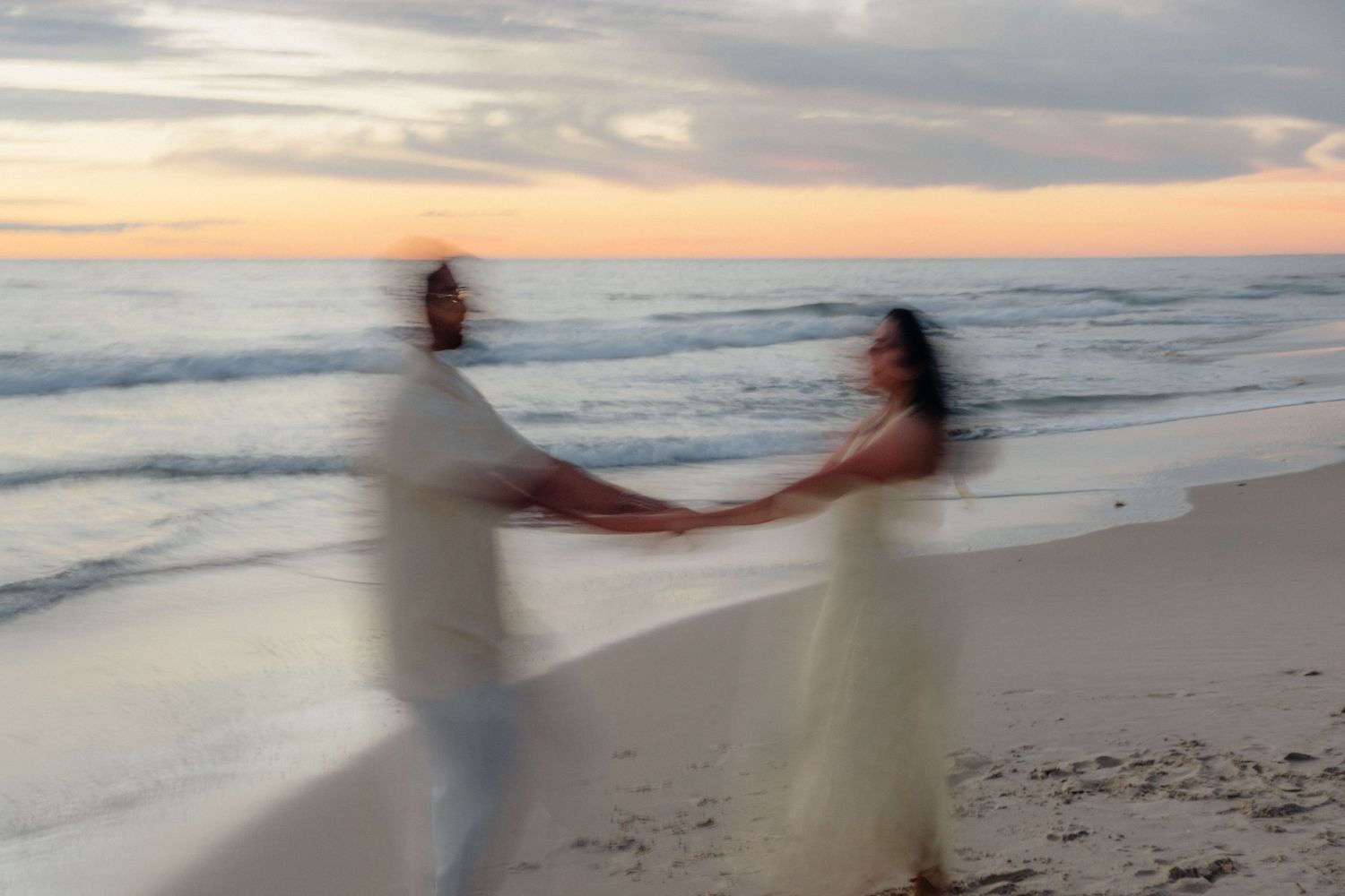 Motion blur artistic photo of couple dancing and holding hands on beach at dusk.