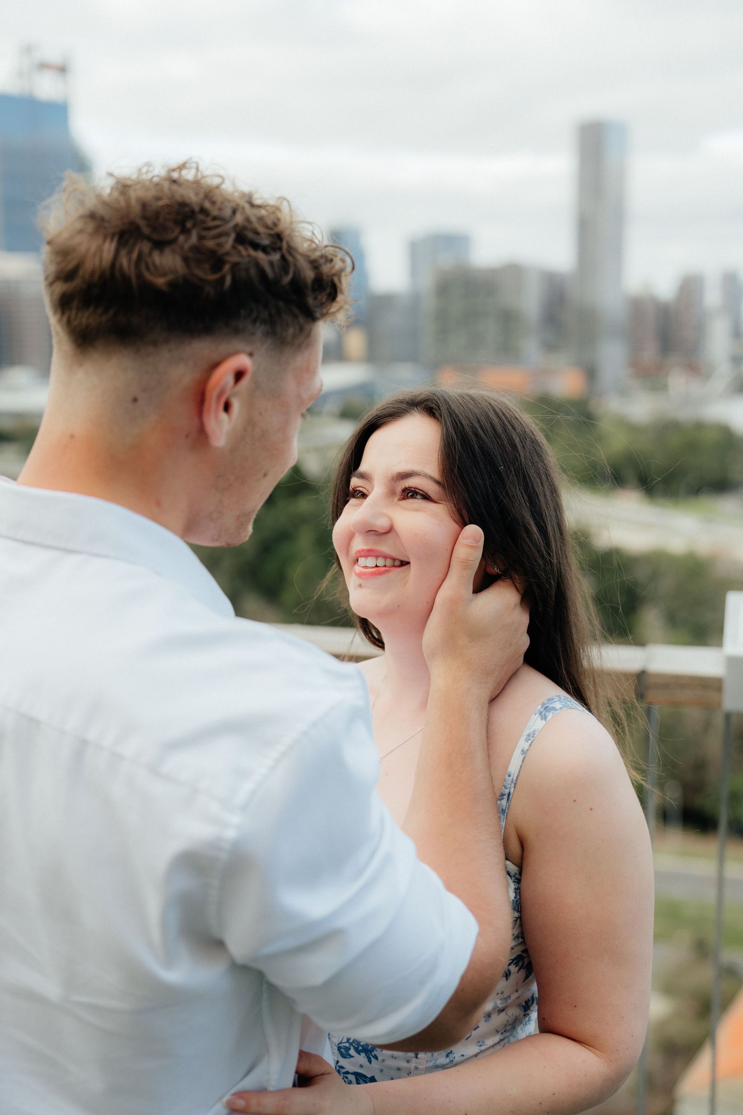 Woman smiling as man gently touches her face with city skyline in the background.