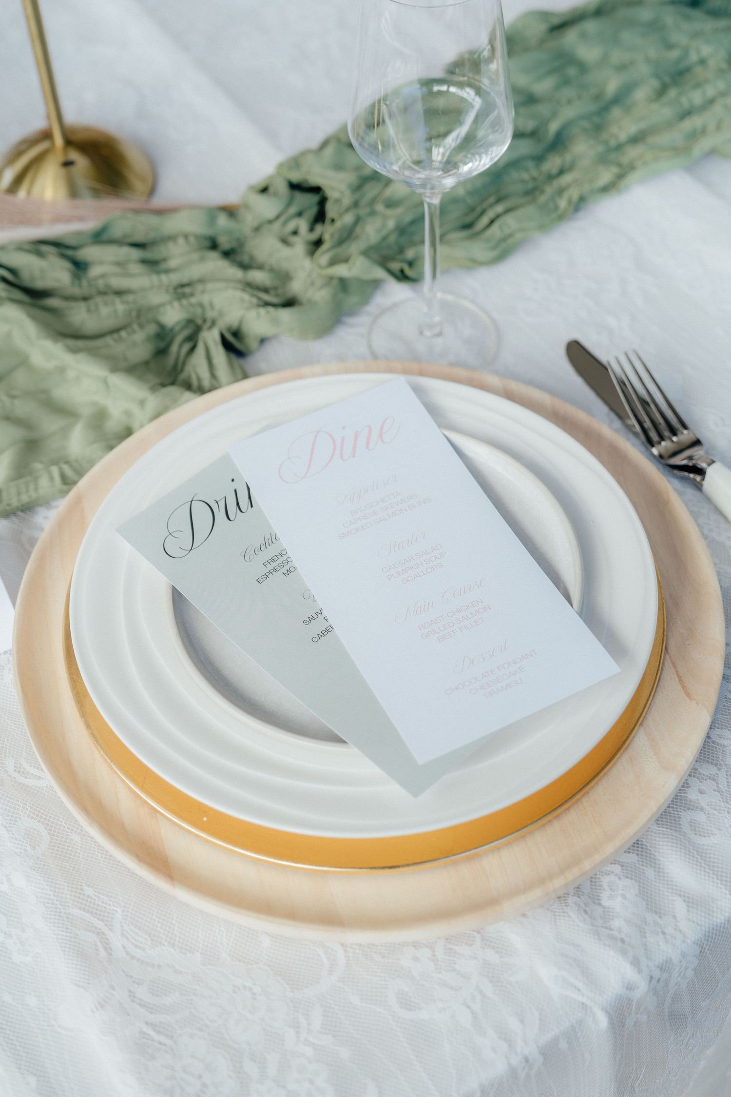 Elegant wedding place setting with gold charger plate, menu cards, and sage green silk ribbon.