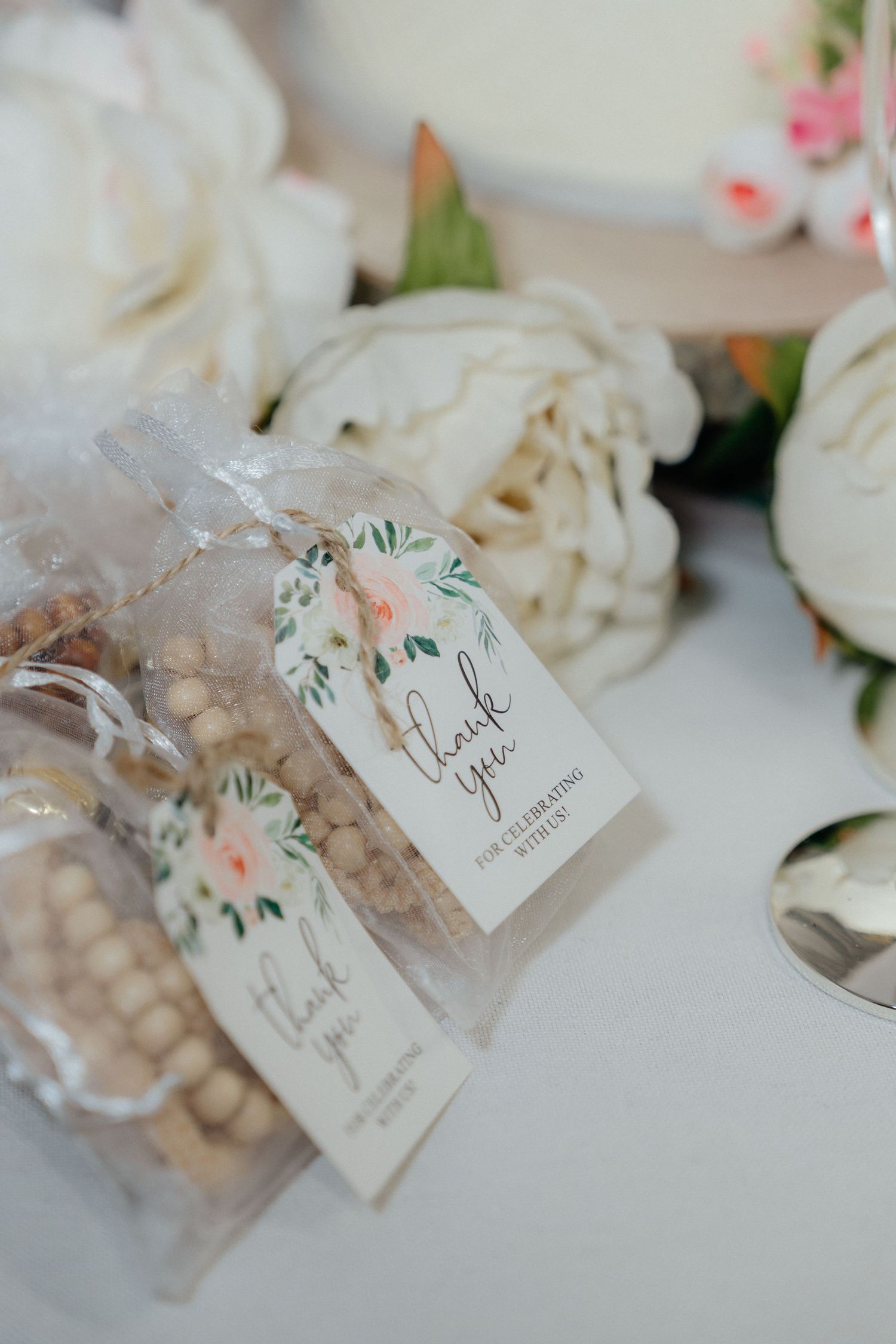Elegant wedding favor bags with thank you tags displayed beside white peonies on a table.