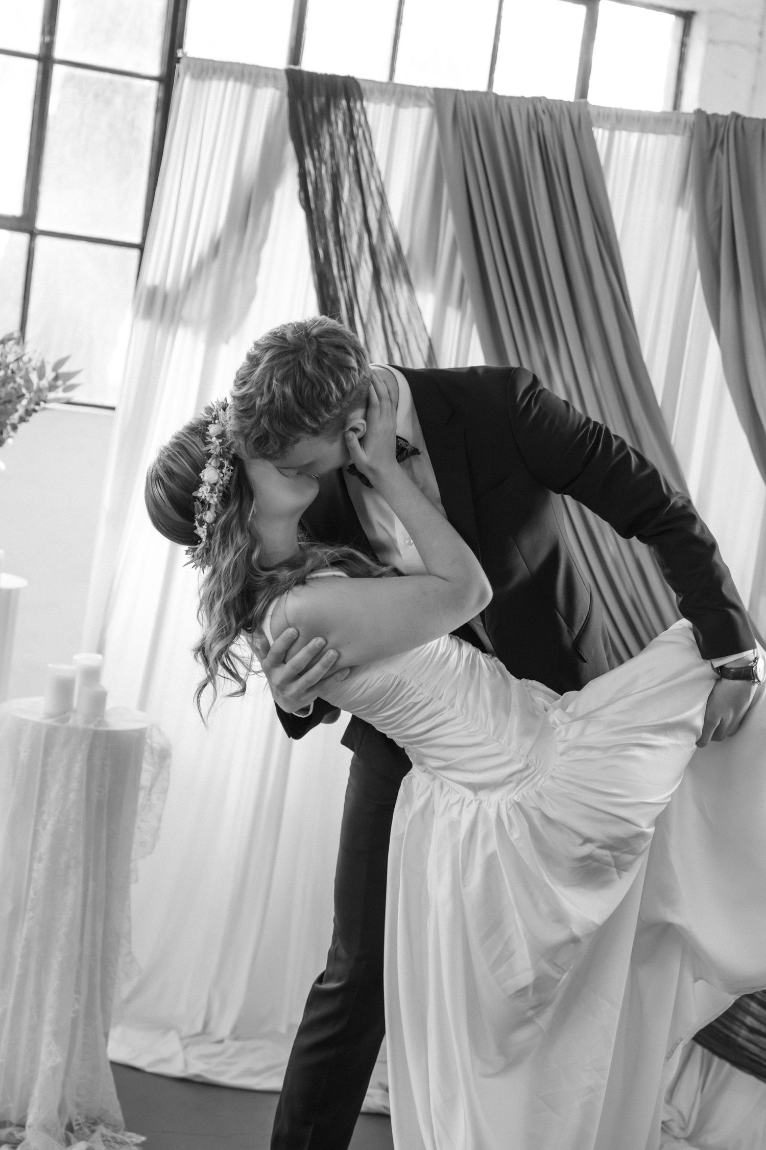 Groom dramatically dips bride for romantic kiss in black and white wedding ceremony photo.