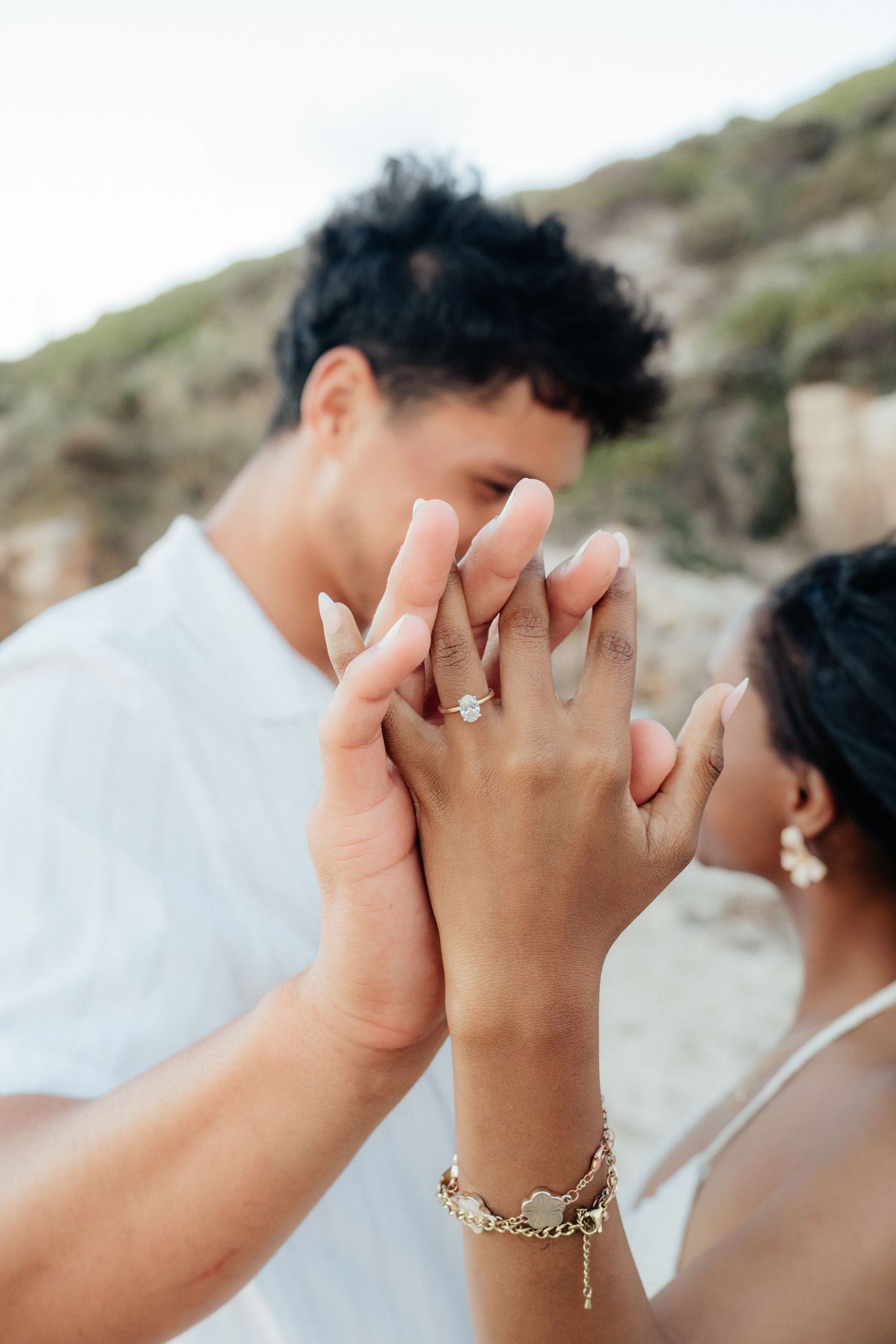 Close-up of couple holding hands displaying a diamond engagement ring and gold bracelet.