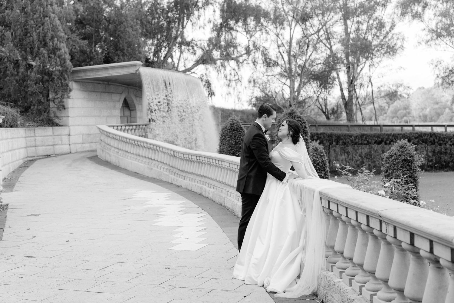Black and white photo of bride and groom embracing on an elegant stone terrace with balustrade.