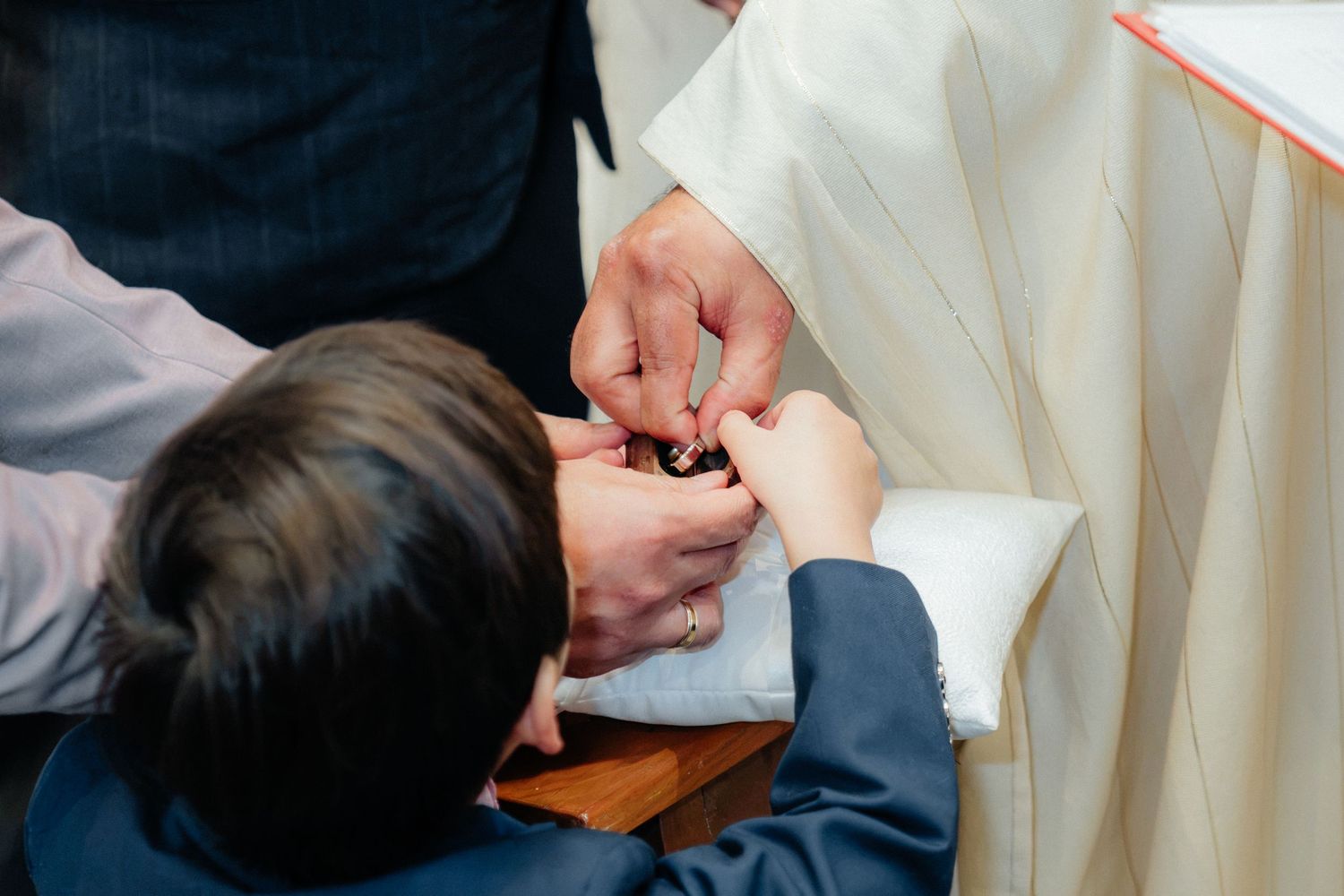 A priest places a wedding ring on a groom's finger during a Catholic wedding ceremony.