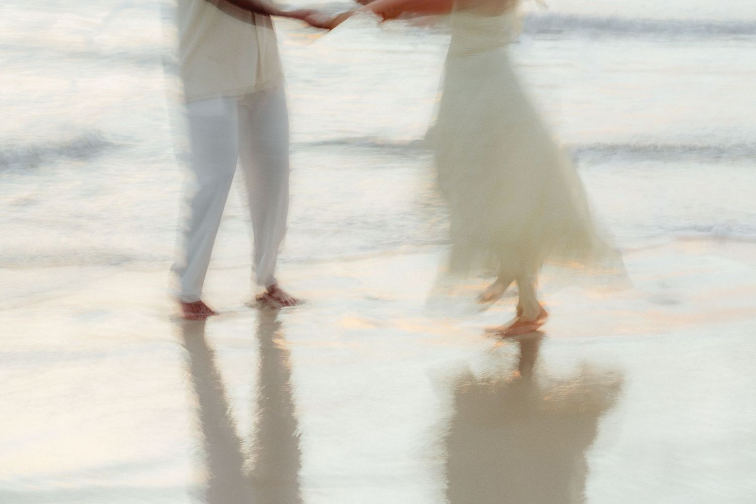 Artistic blurred reflection of couple holding hands on wet beach sand at sunset.