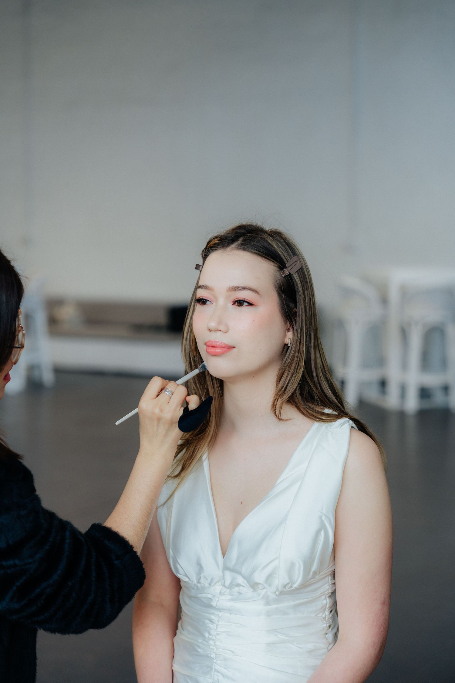 Makeup artist applying lipstick to beautiful bride in white wedding dress before ceremony.