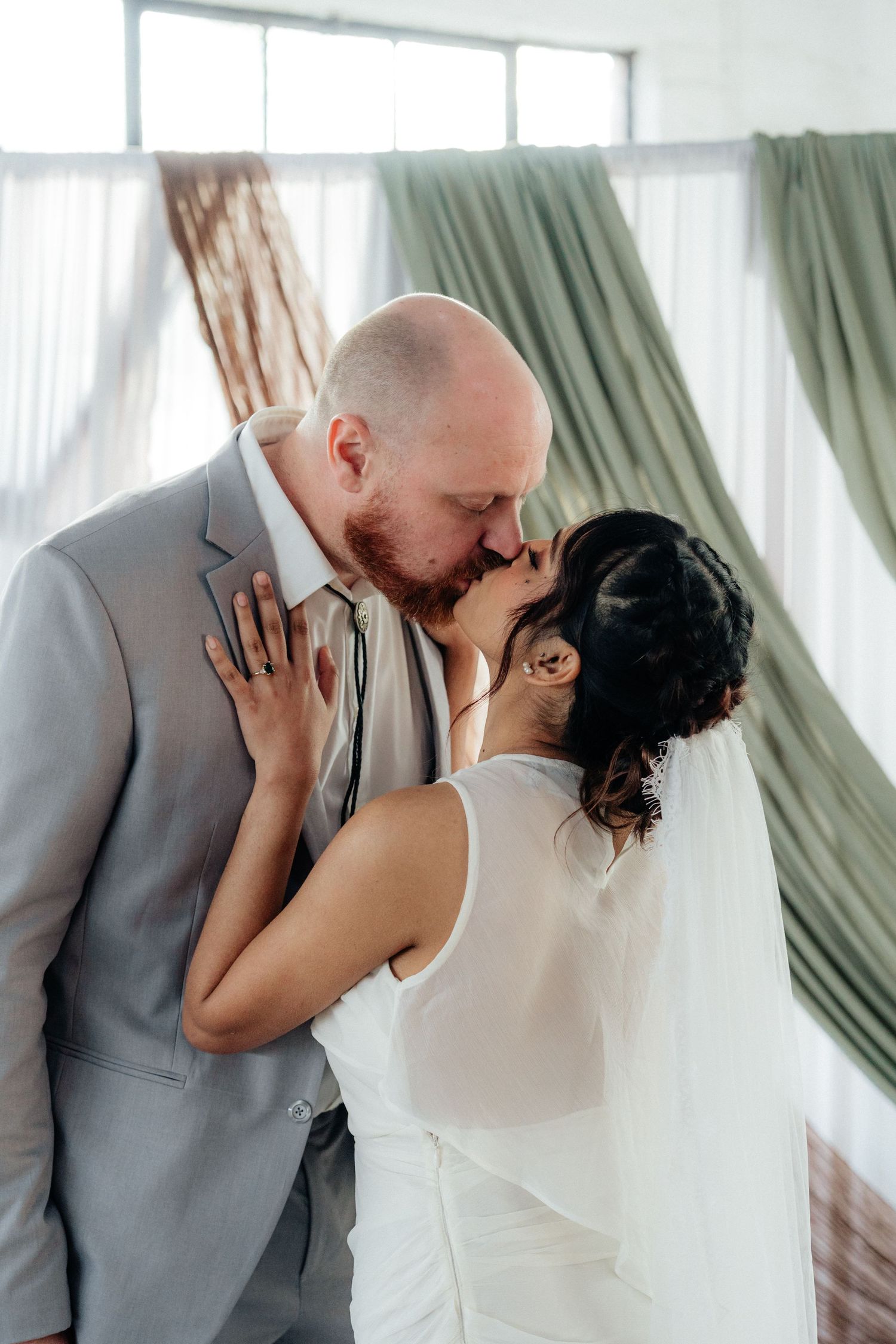Bride and groom sharing their first kiss at the wedding altar with green drapes.