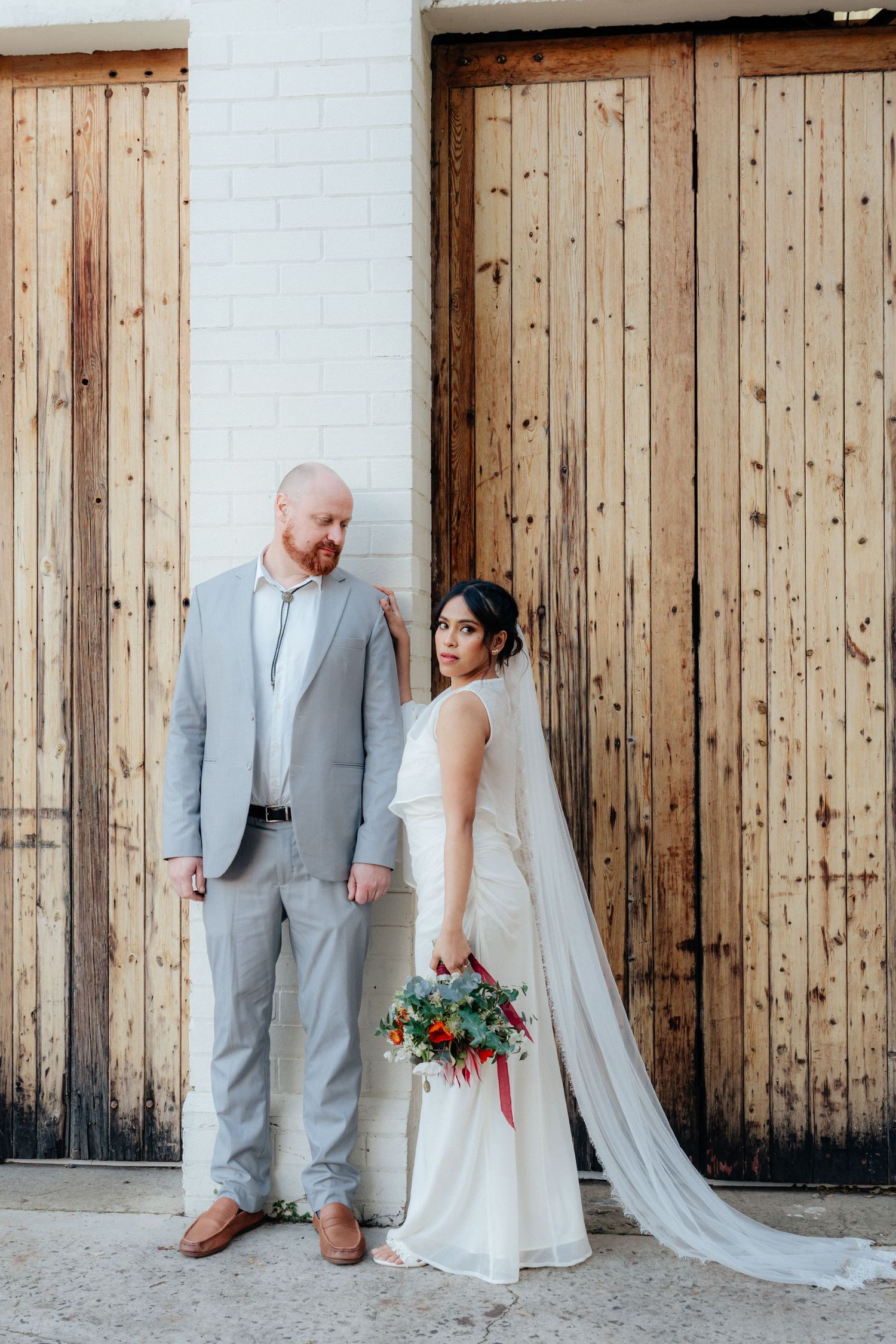 Bride and groom posing together in front of rustic wooden doors after their wedding.