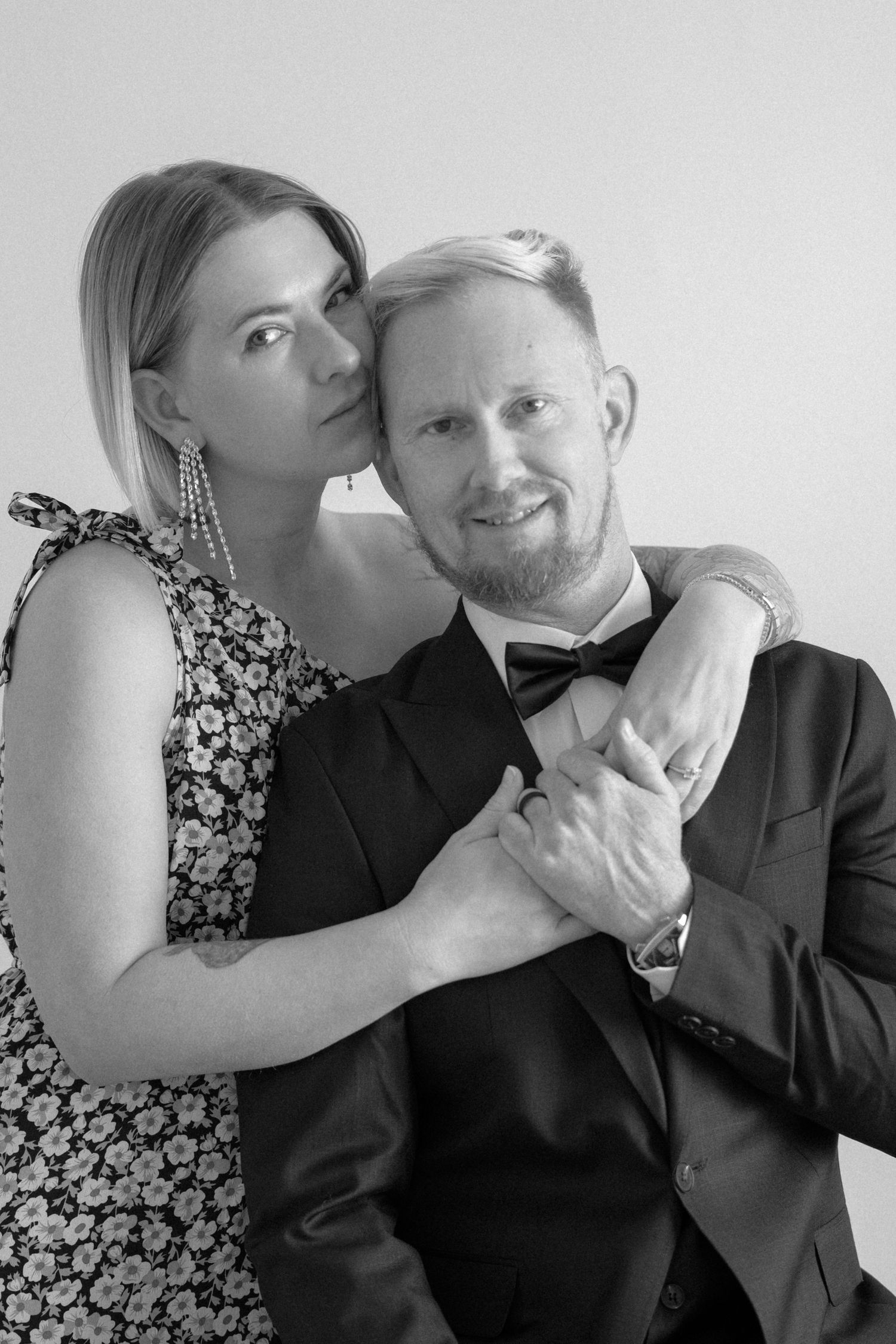 Black and white portrait of couple embracing, woman in floral dress and man in tuxedo.