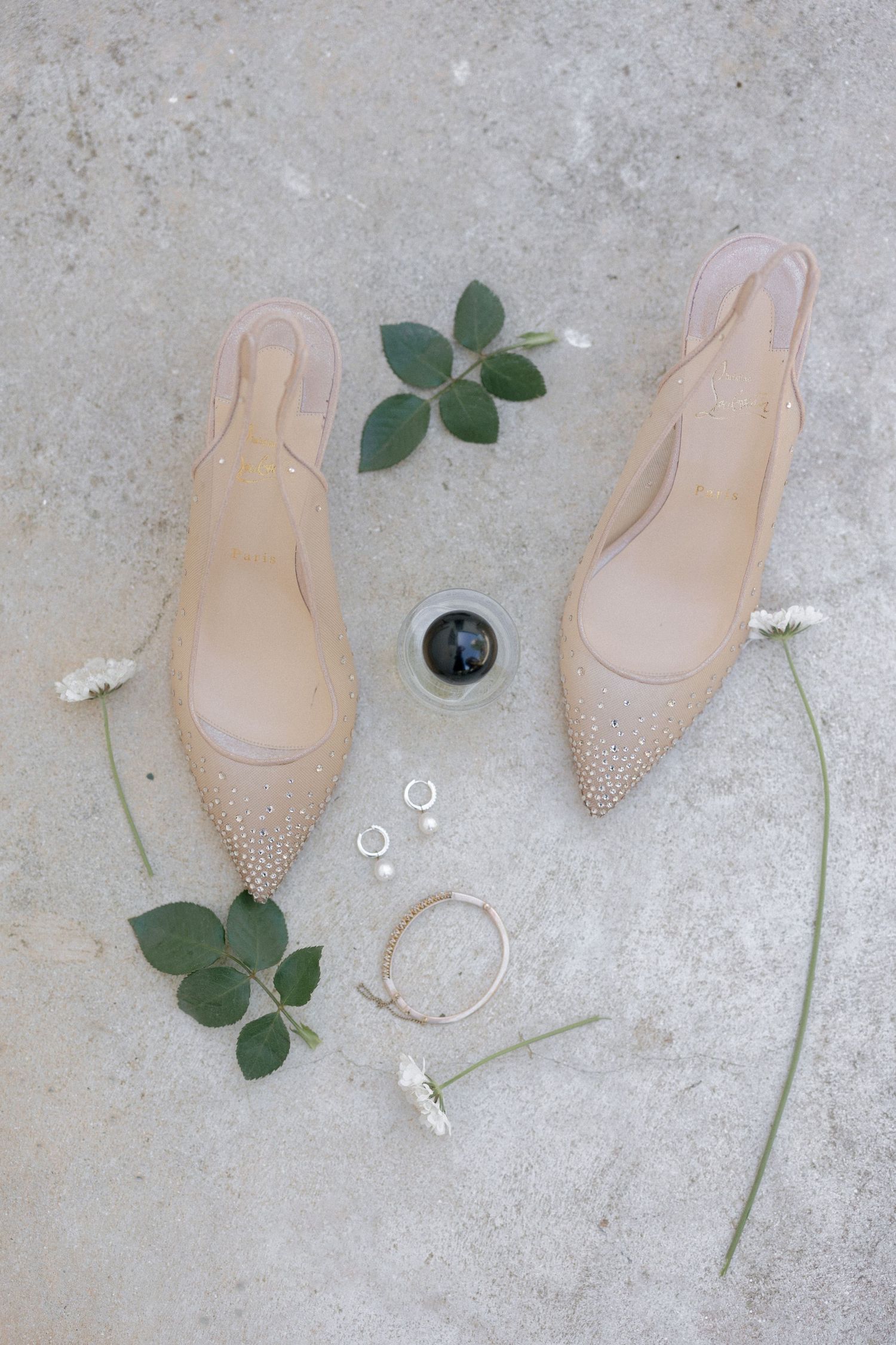 Flat lay of nude bridal heels with pearl details surrounded by jewelry and white flowers.