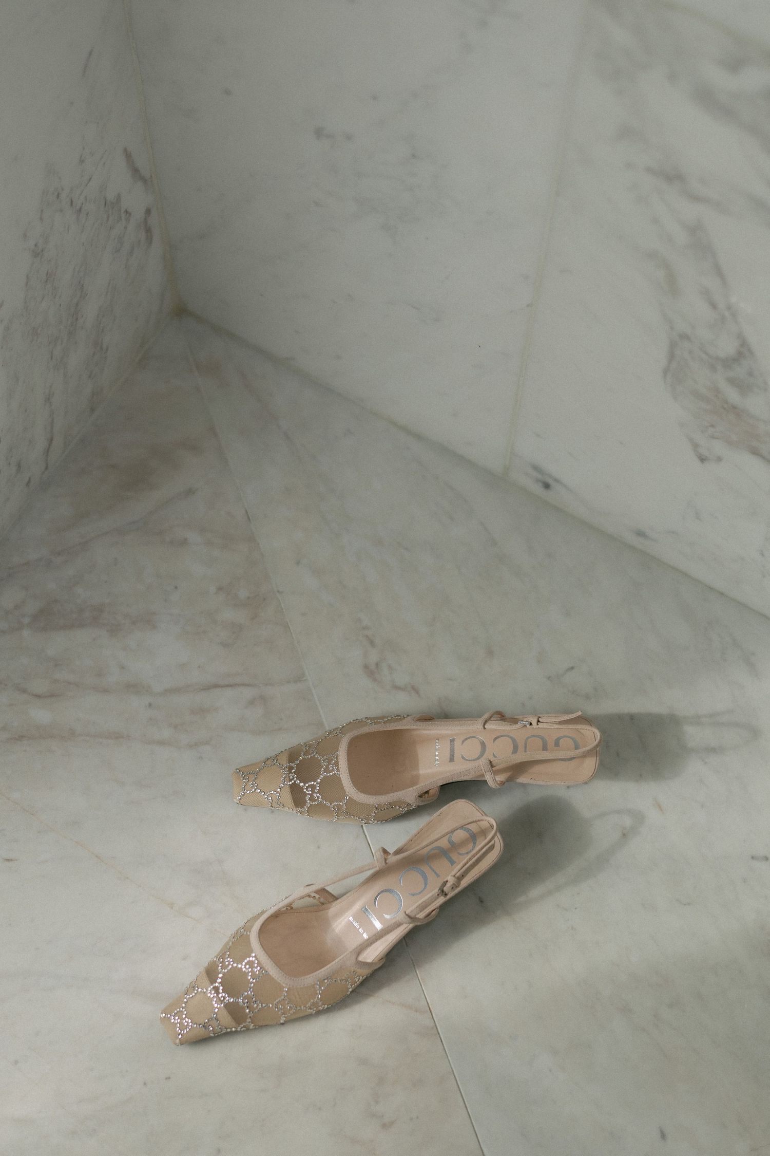 Beige Gucci slingback heels with GG monogram pattern displayed on white marble floor.