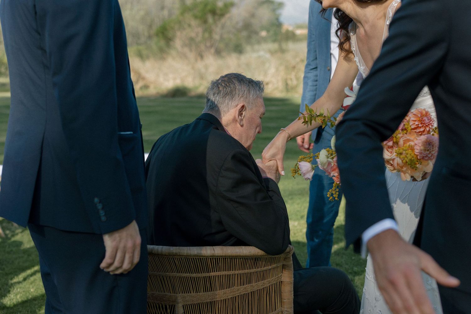 Wedding guest seated on barrel during outdoor ceremony while bride and groom stand nearby.