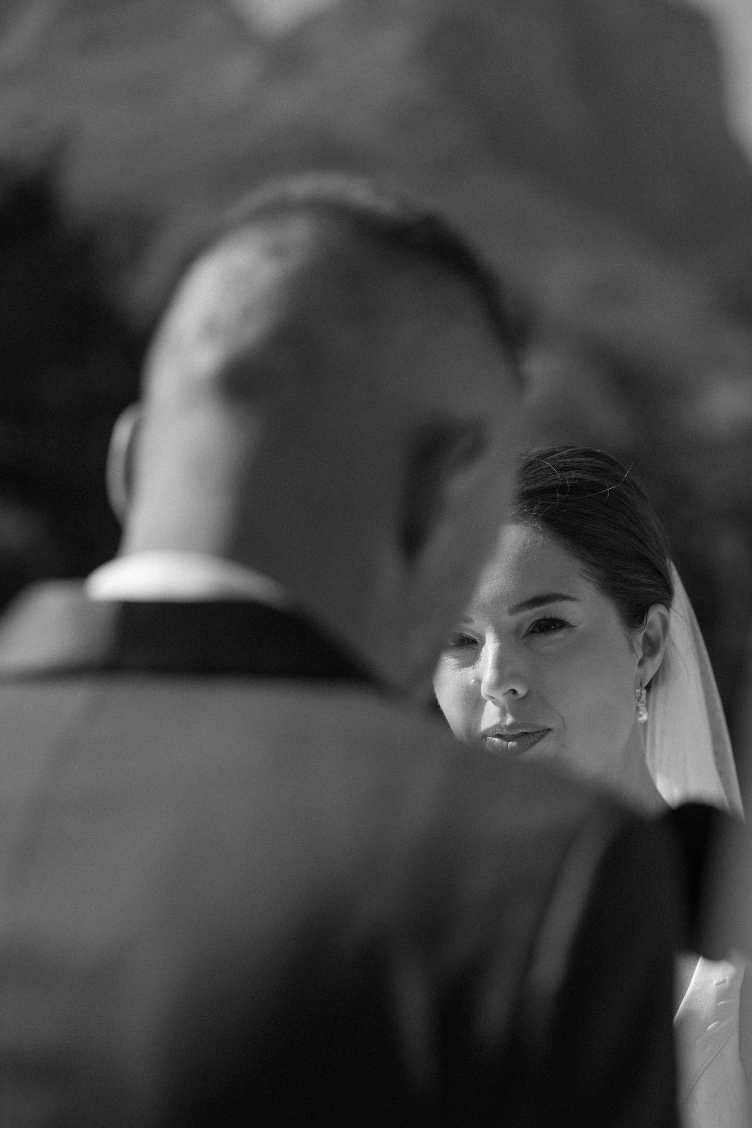Black and white wedding photo of bride gazing lovingly at groom during outdoor ceremony.
