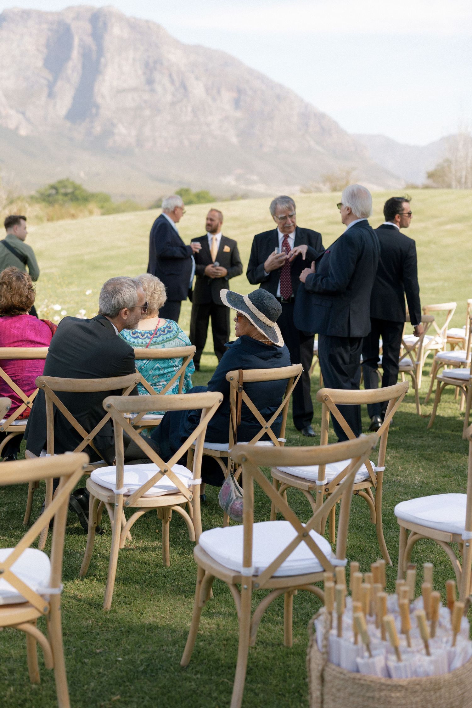 Wedding guests seated in wooden cross-back chairs at outdoor ceremony with stunning mountain landscape background.