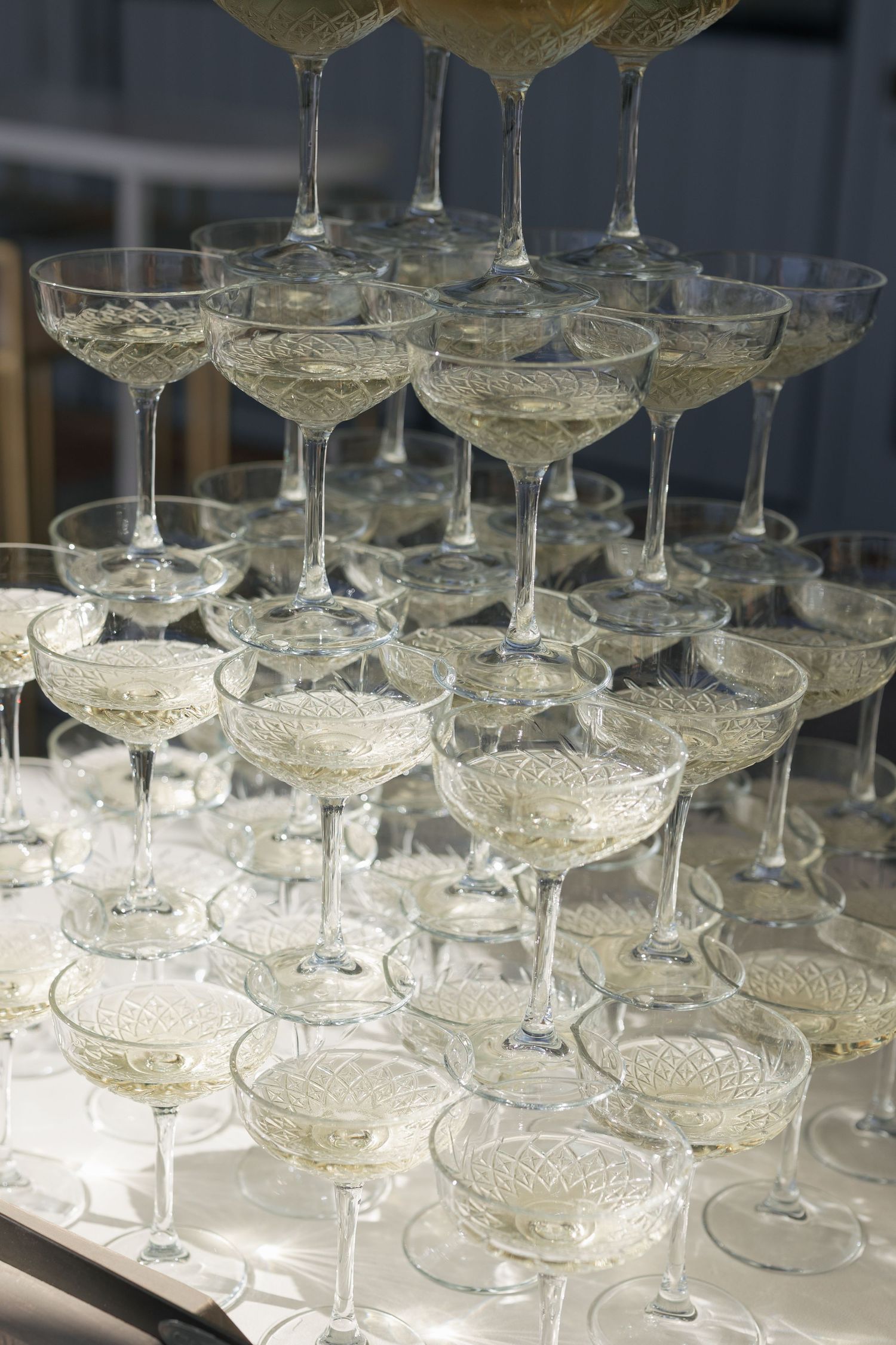 Close-up of elegant crystal champagne coupe glasses stacked in pyramid tower at wedding reception.