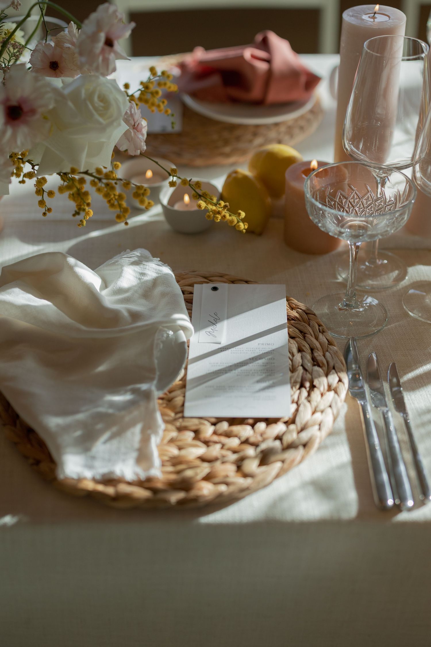 Wedding table setting with woven charger, white napkin, crystal glass, and yellow flowers.