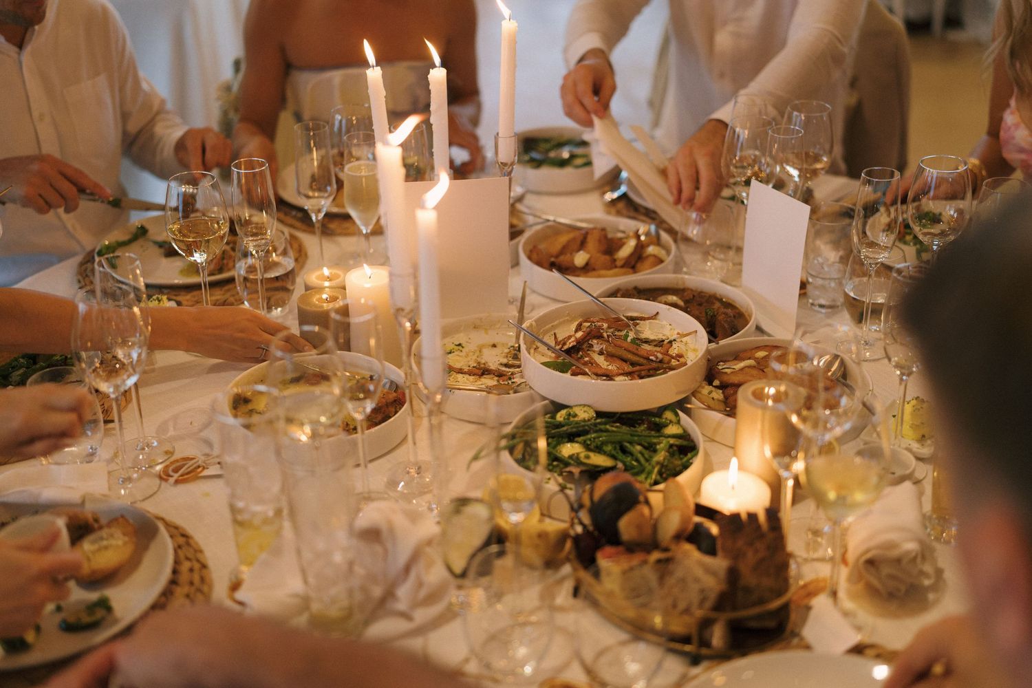 Elegant candlelit dinner party table with wine glasses, fresh dishes, and guests dining together in warm ambient light.