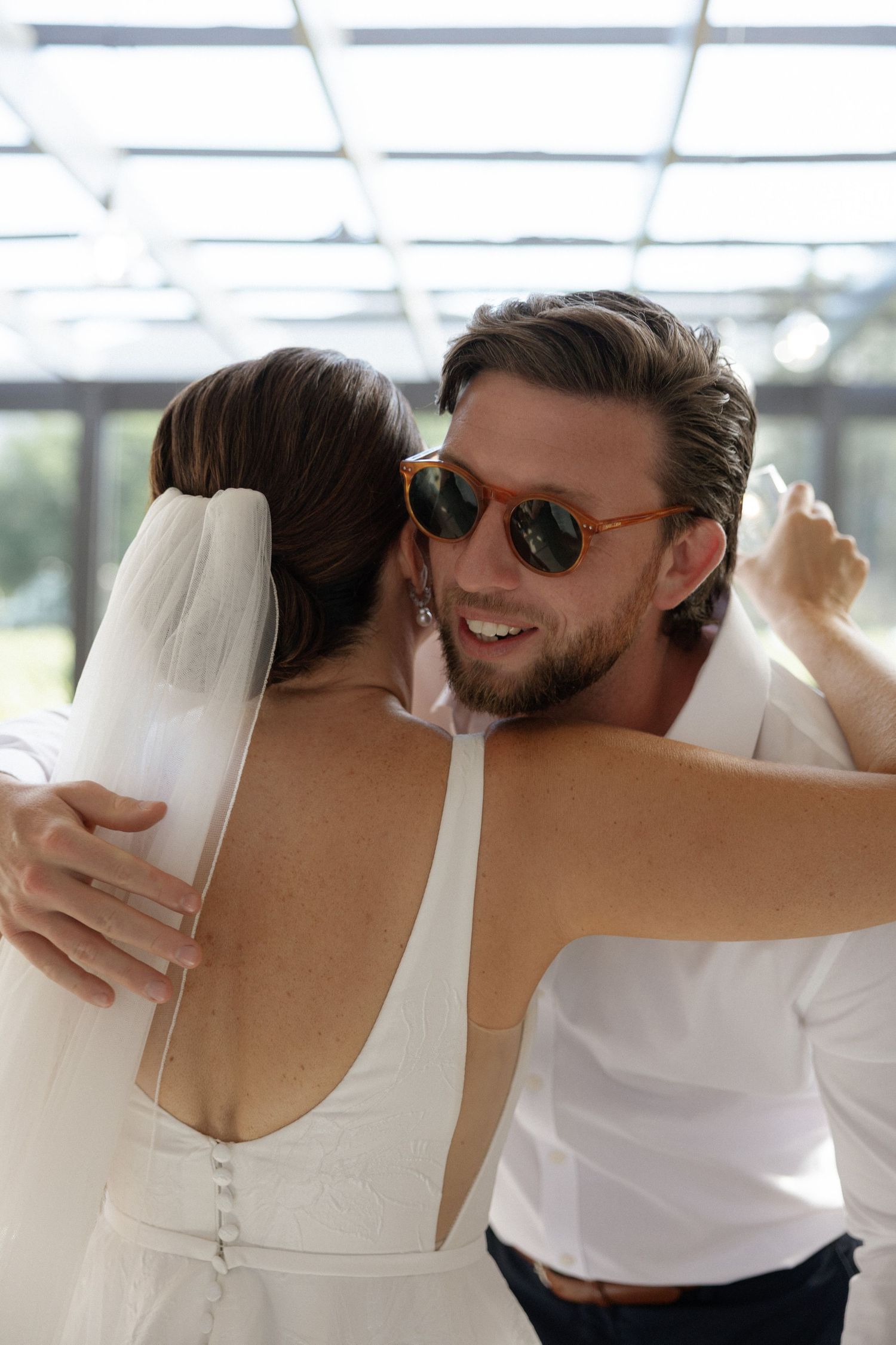 Smiling groom in sunglasses embracing bride in white wedding dress during their first dance.