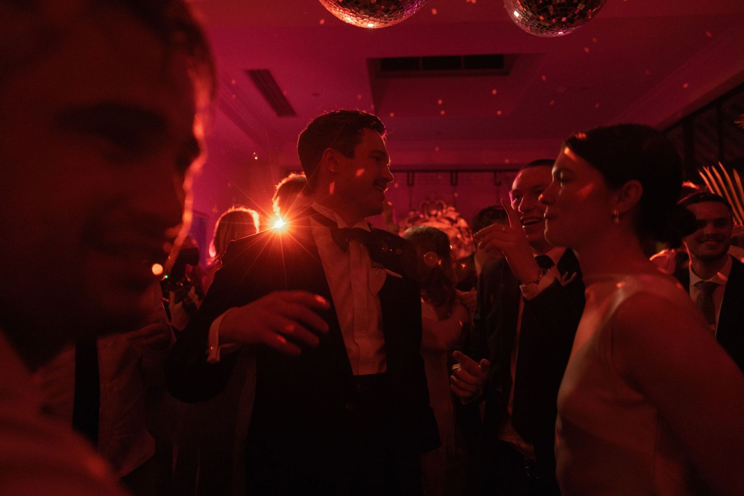 bridal Couple sharing a romantic dance at a wedding reception under red lights and a disco ball.