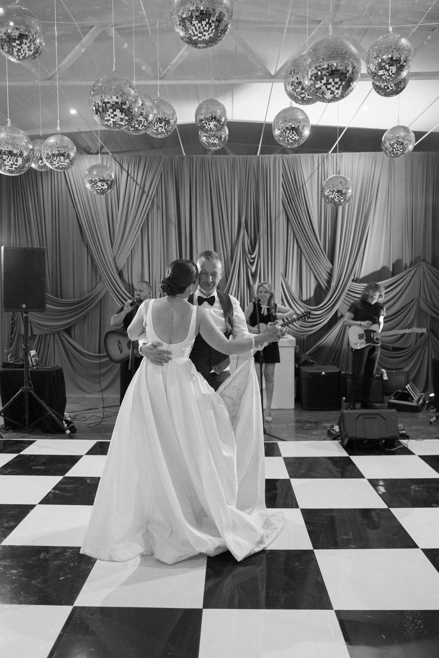 Bride and groom share first dance on checkered floor under disco balls at wedding reception.