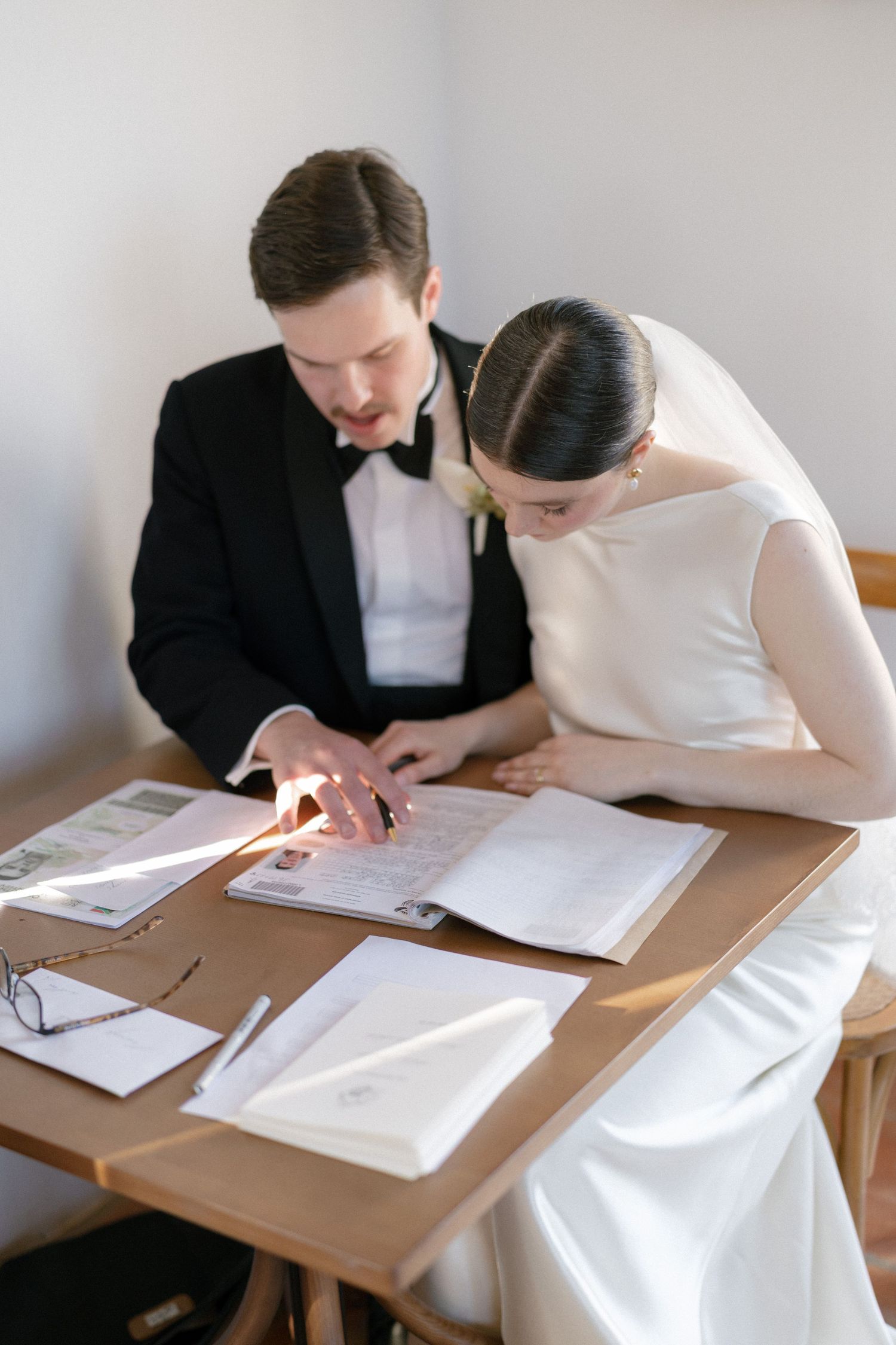 Bride and groom reviewing and signing official wedding documents together at wooden table during ceremony.