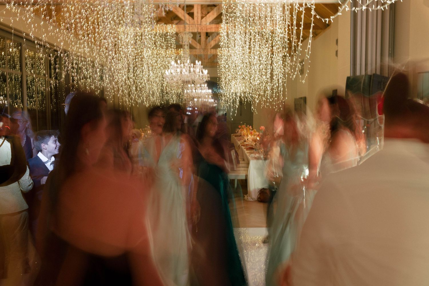Motion blur captures wedding guests dancing beneath cascading fairy lights at reception.