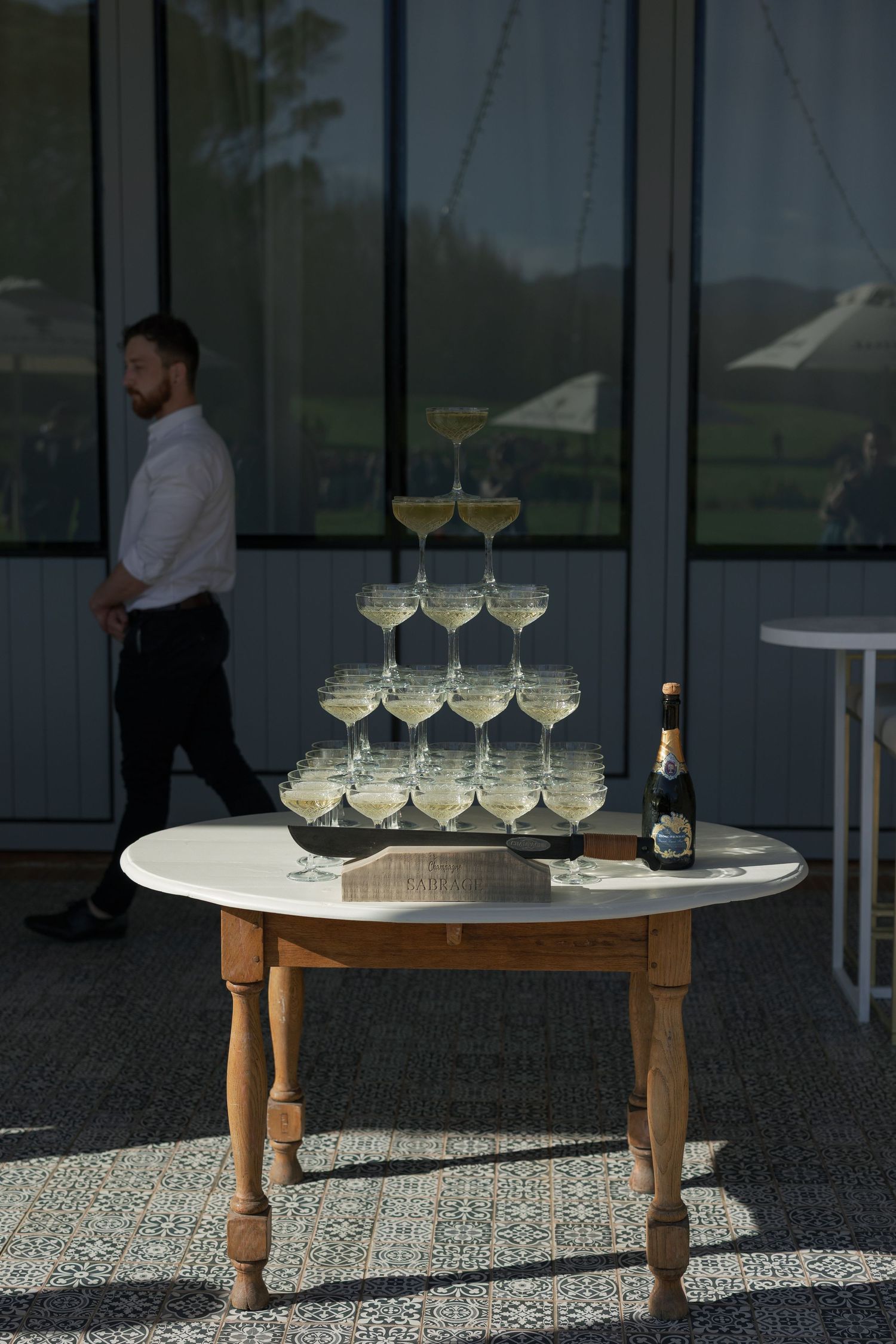 Elegant champagne tower on wooden table with bottle beside it at wedding reception venue.