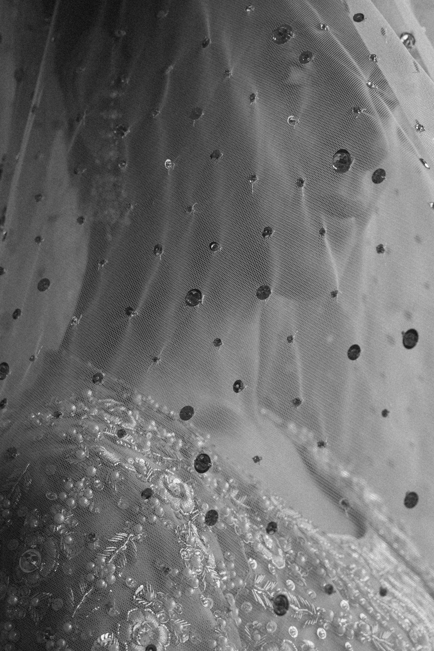 Close-up black and white photo of a bridal veil with sequin dots over embroidered lace wedding dress fabric.