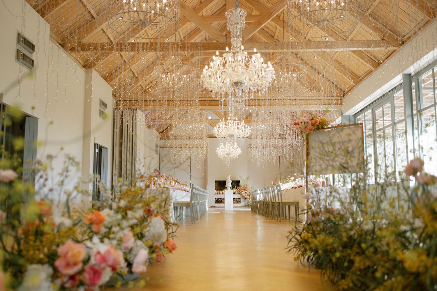 Elegant wedding venue with crystal chandeliers, hanging lights, and floral aisle arrangements.