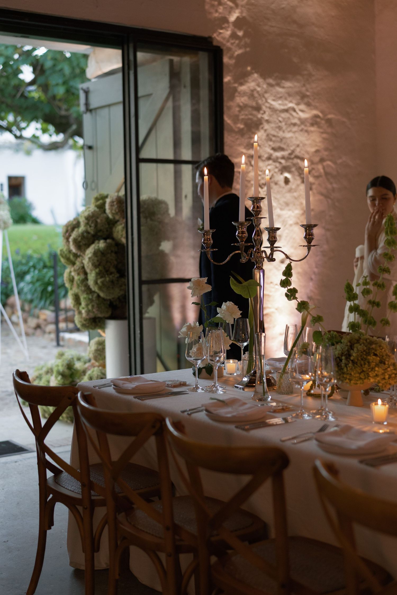 Elegant wedding reception table set with candelabras, glassware, and greenery floral arrangements.