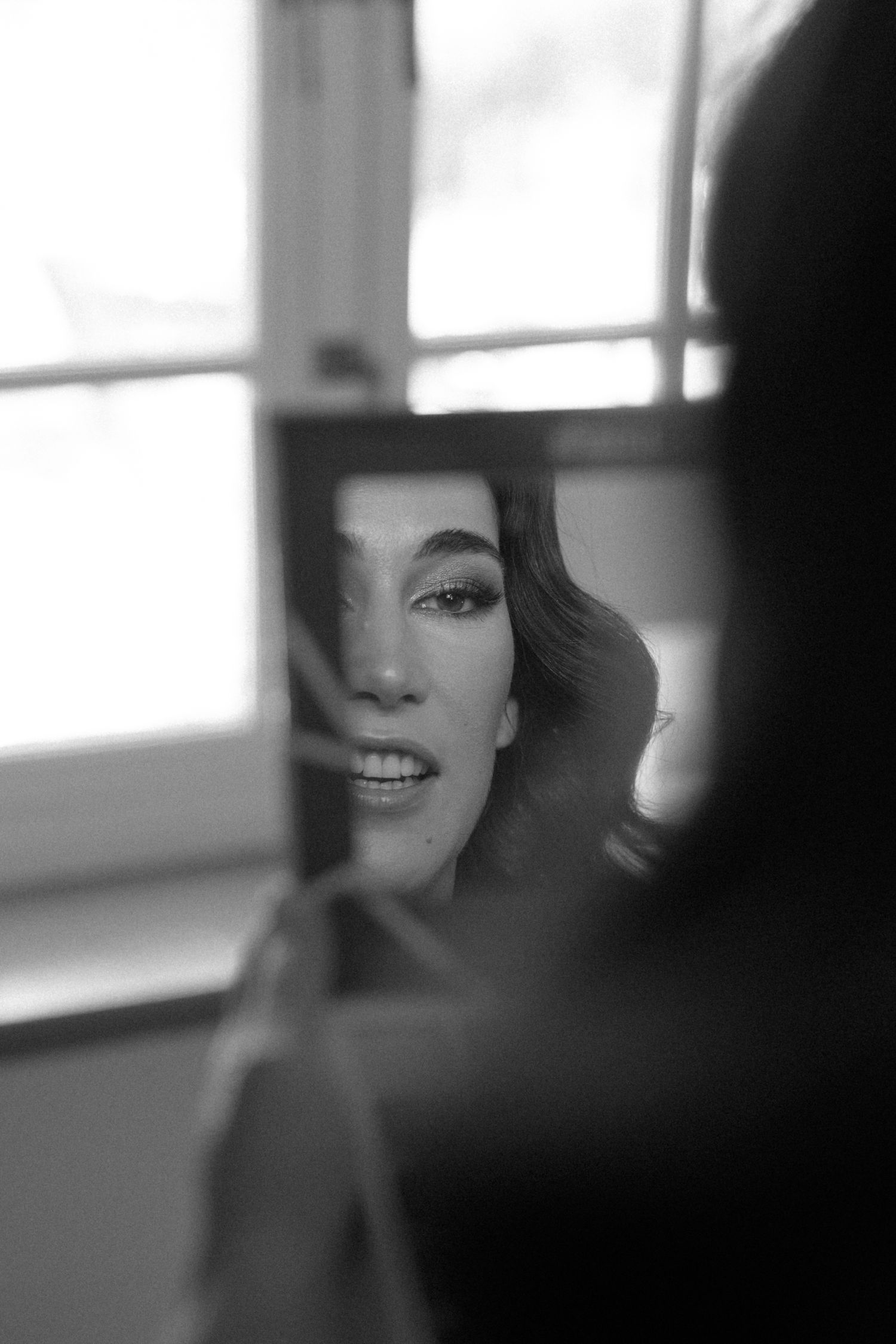 Black and white portrait of a bride's reflection in a mirror during wedding makeup application.