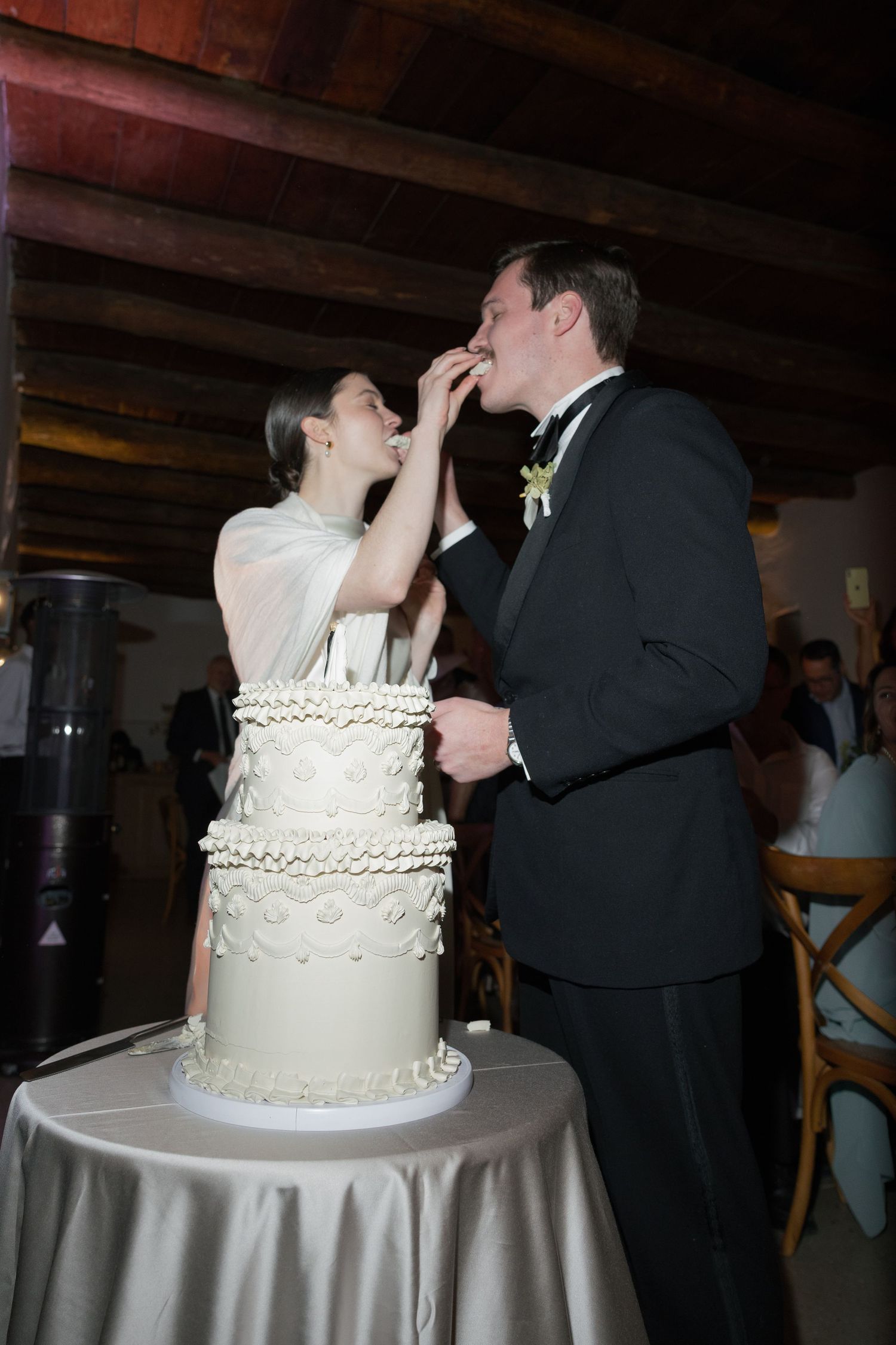 Bride and groom sharing wedding cake cutting moment, feeding each other at their elegant white tiered cake.