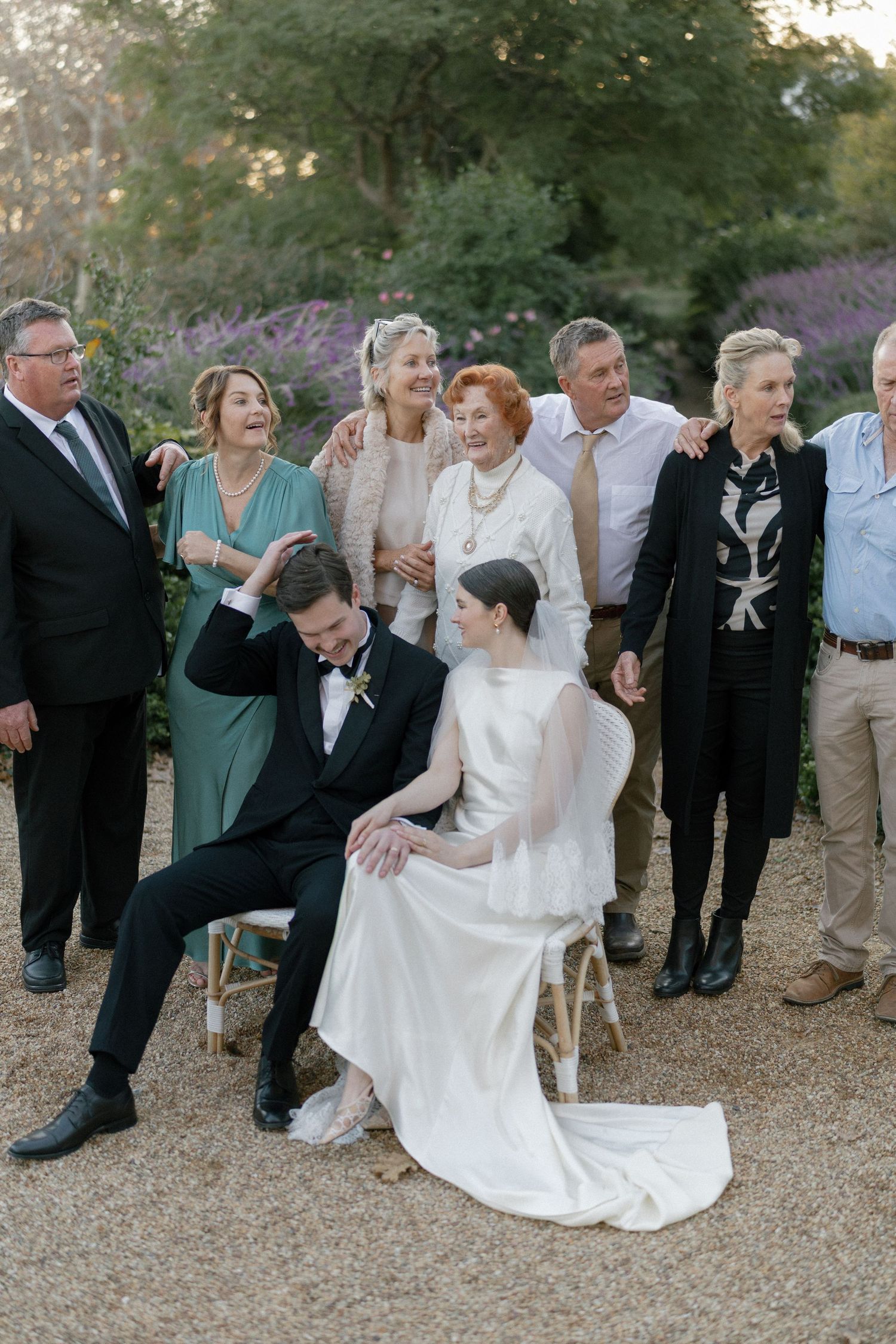 Wedding couple seated with family group portrait in a garden setting during golden hour.