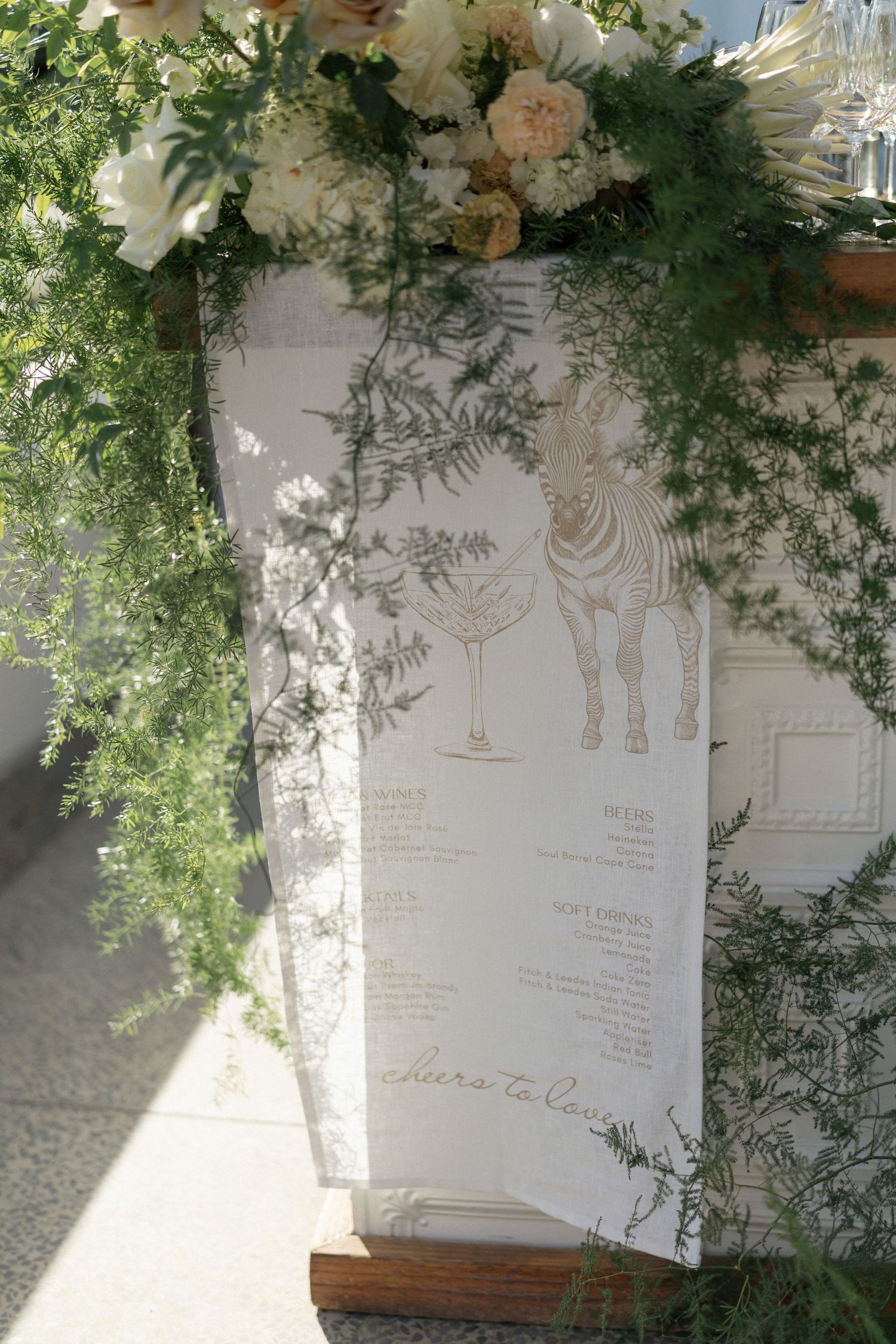 Elegant wedding menu display with zebra illustration, surrounded by lush greenery and white floral arrangements.