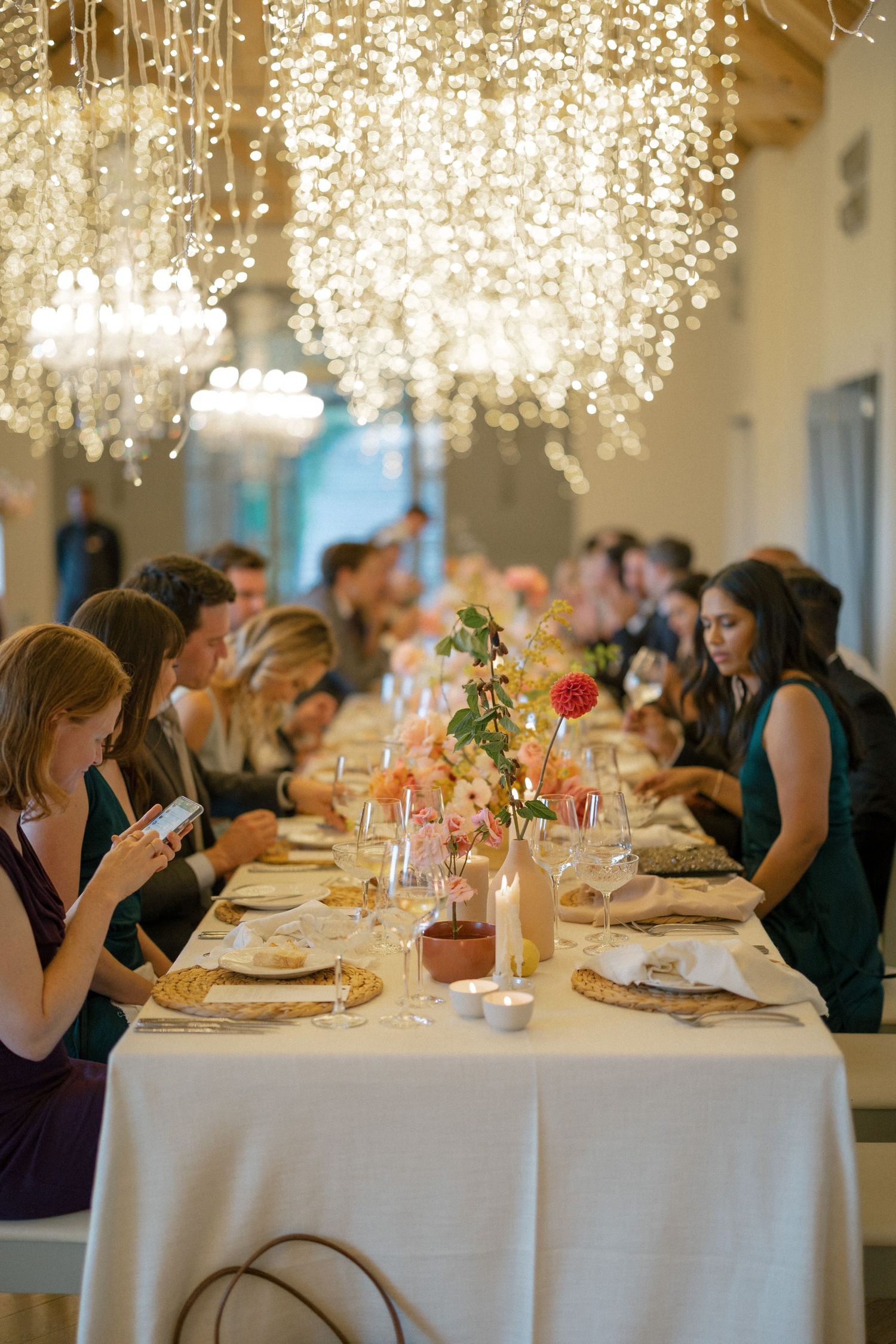 Elegant wedding reception dinner table with floral centerpieces under crystal chandeliers.