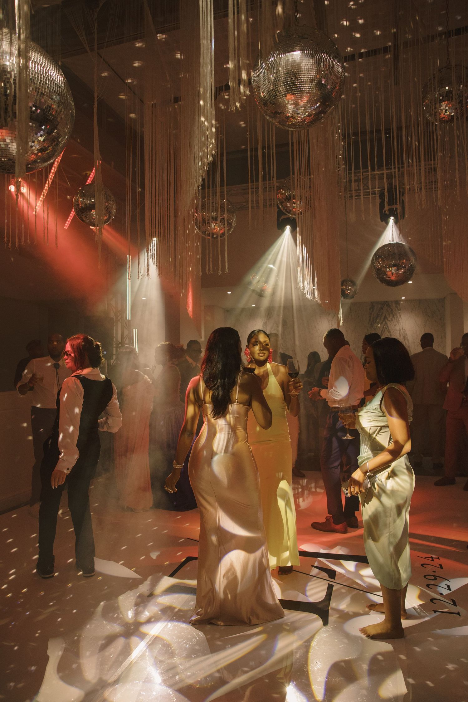 Elegant wedding reception with disco balls, glowing lights, and guests in formal attire dancing on a dance floor.