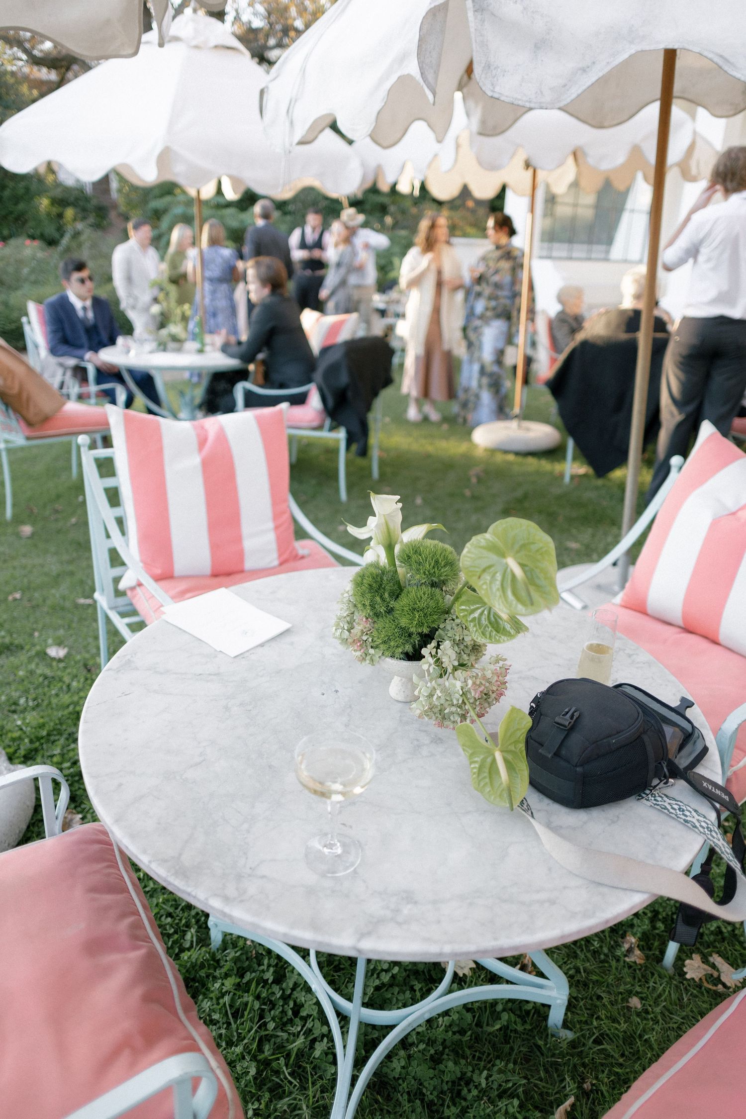 Elegant outdoor wedding reception with pink striped chairs, marble tables, and striped umbrellas on green lawn.