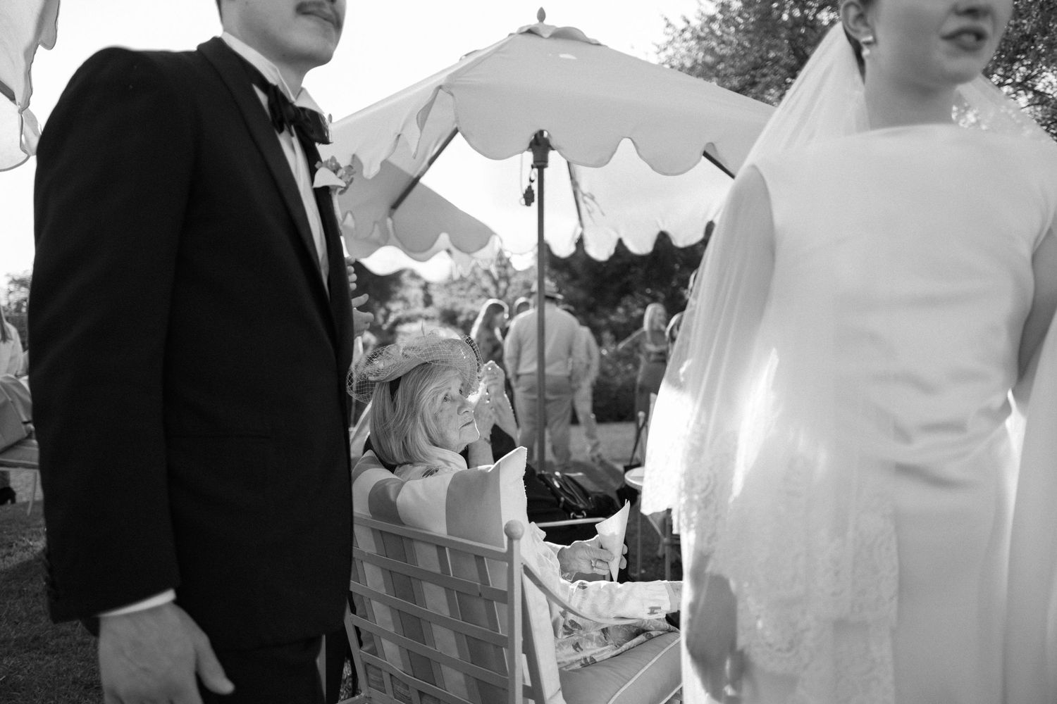 Black and white wedding photo of bride and groom at outdoor ceremony with guests seated under a tent.