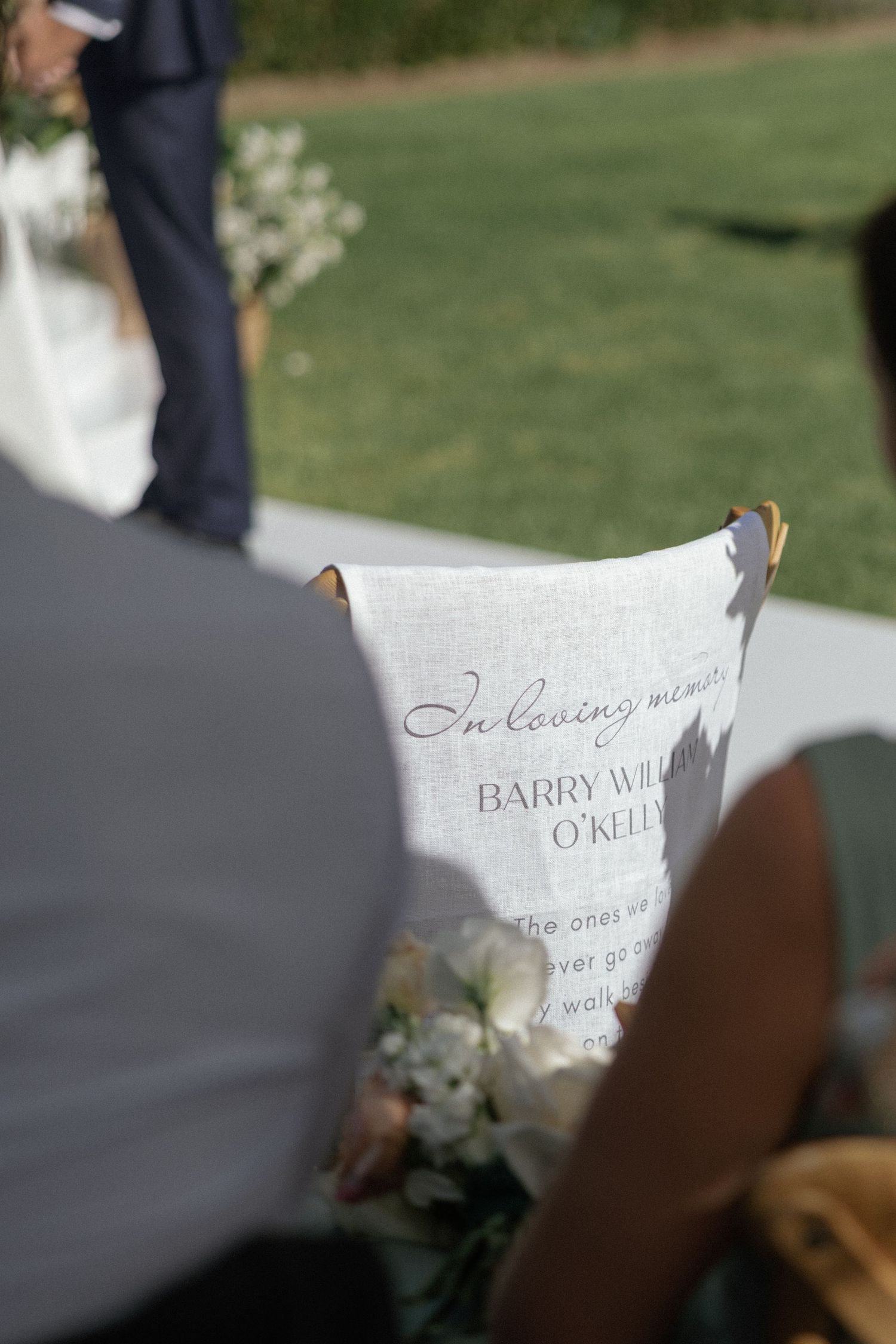 A memorial sign reading In Loving Memory of Barry William O'Kelly displayed at an outdoor wedding ceremony.