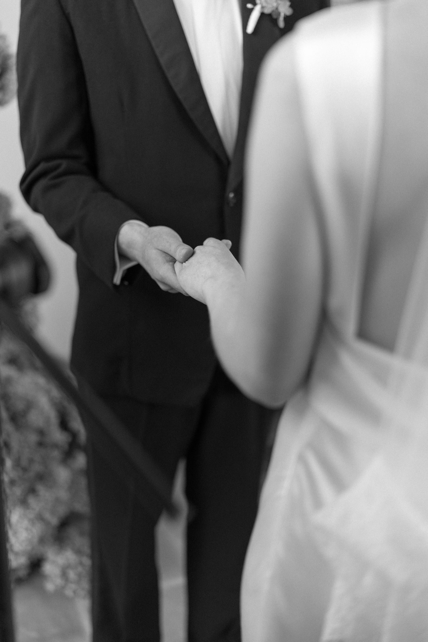 Black and white photo of bride and groom holding hands during wedding ceremony.